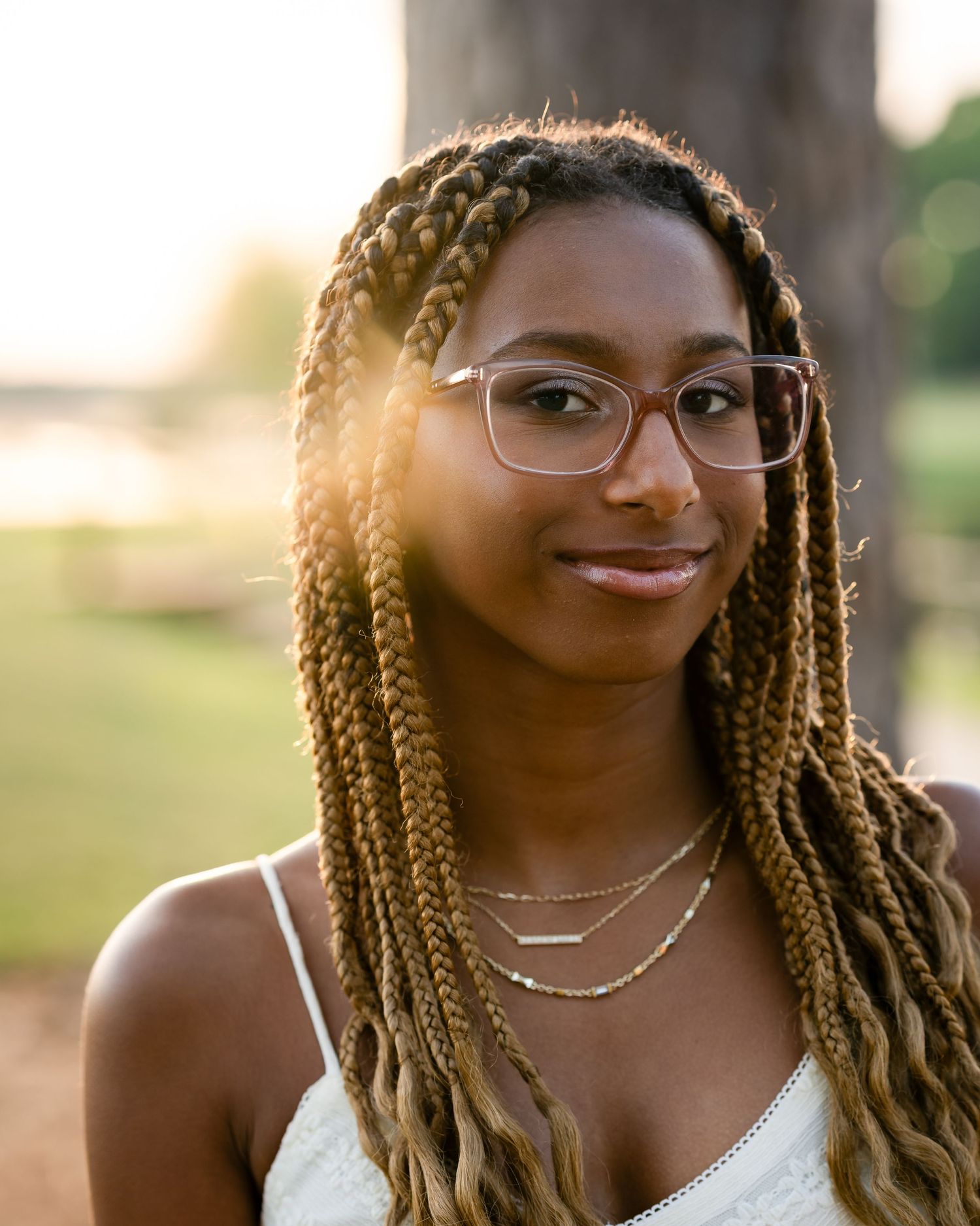 Close-up portrait highlighting braided hairstyle and glasses in warm sunlight.