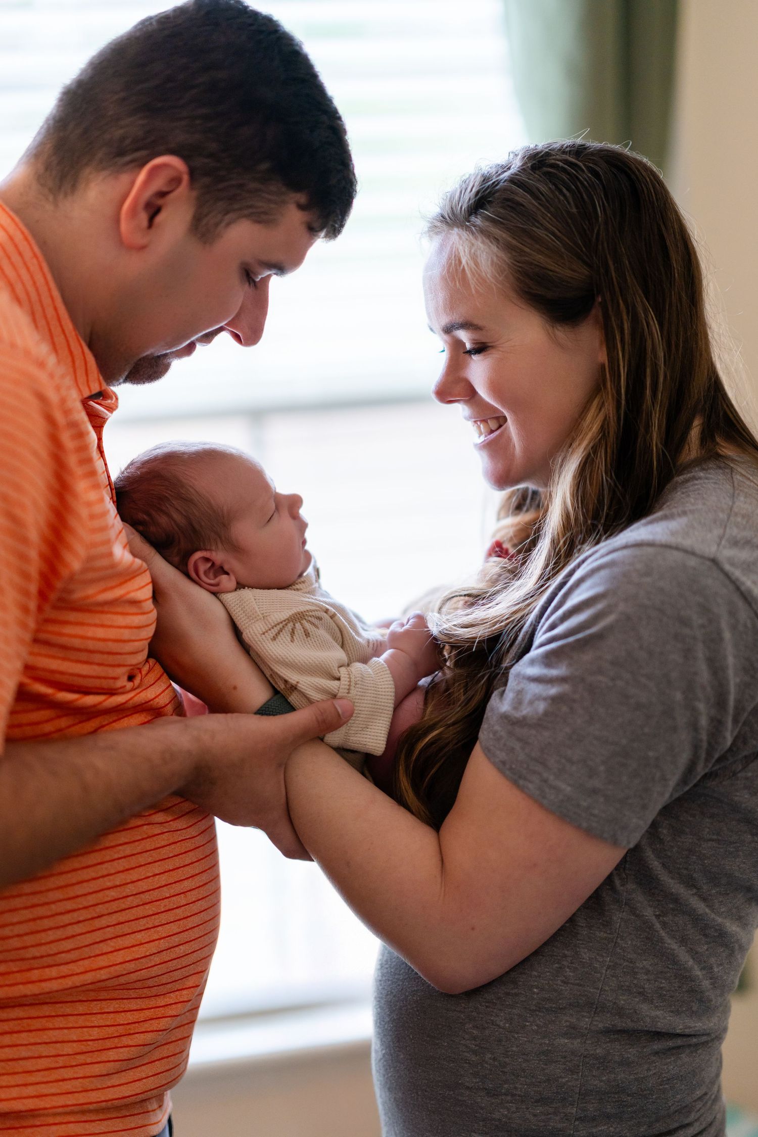 Parents in casual attire lovingly holding their newborn baby.