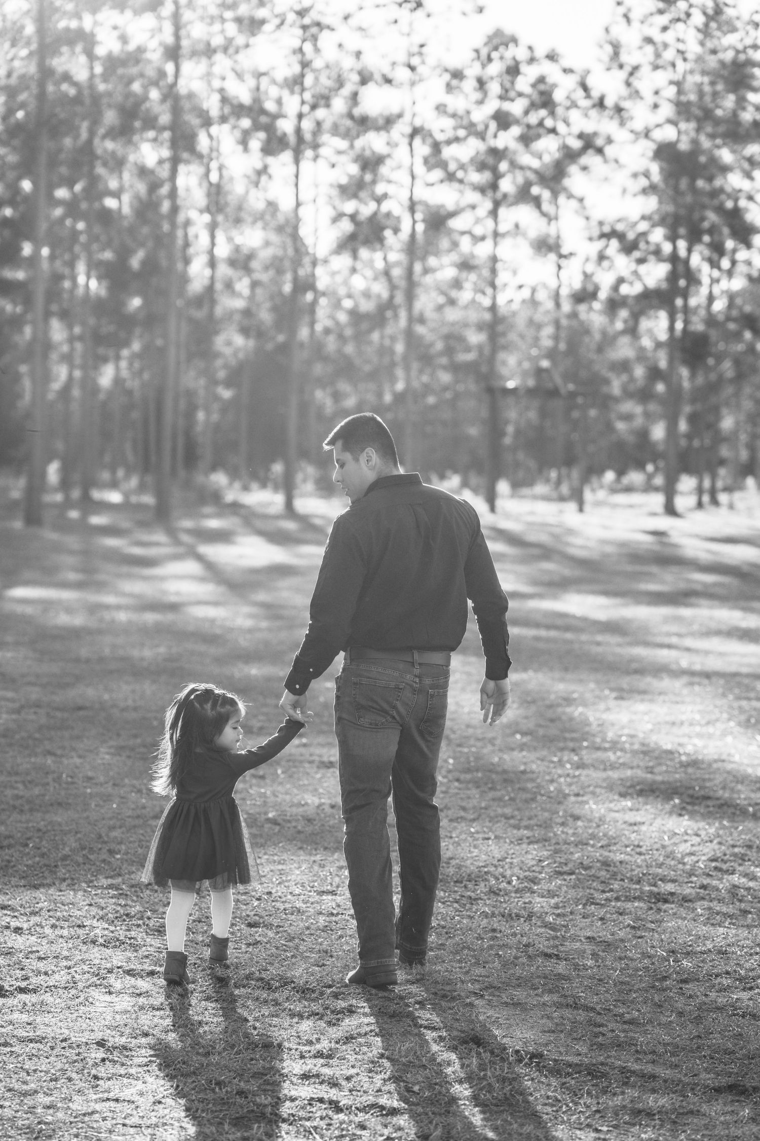 A black and white capture of family members walking together through a sunlit outdoor setting.