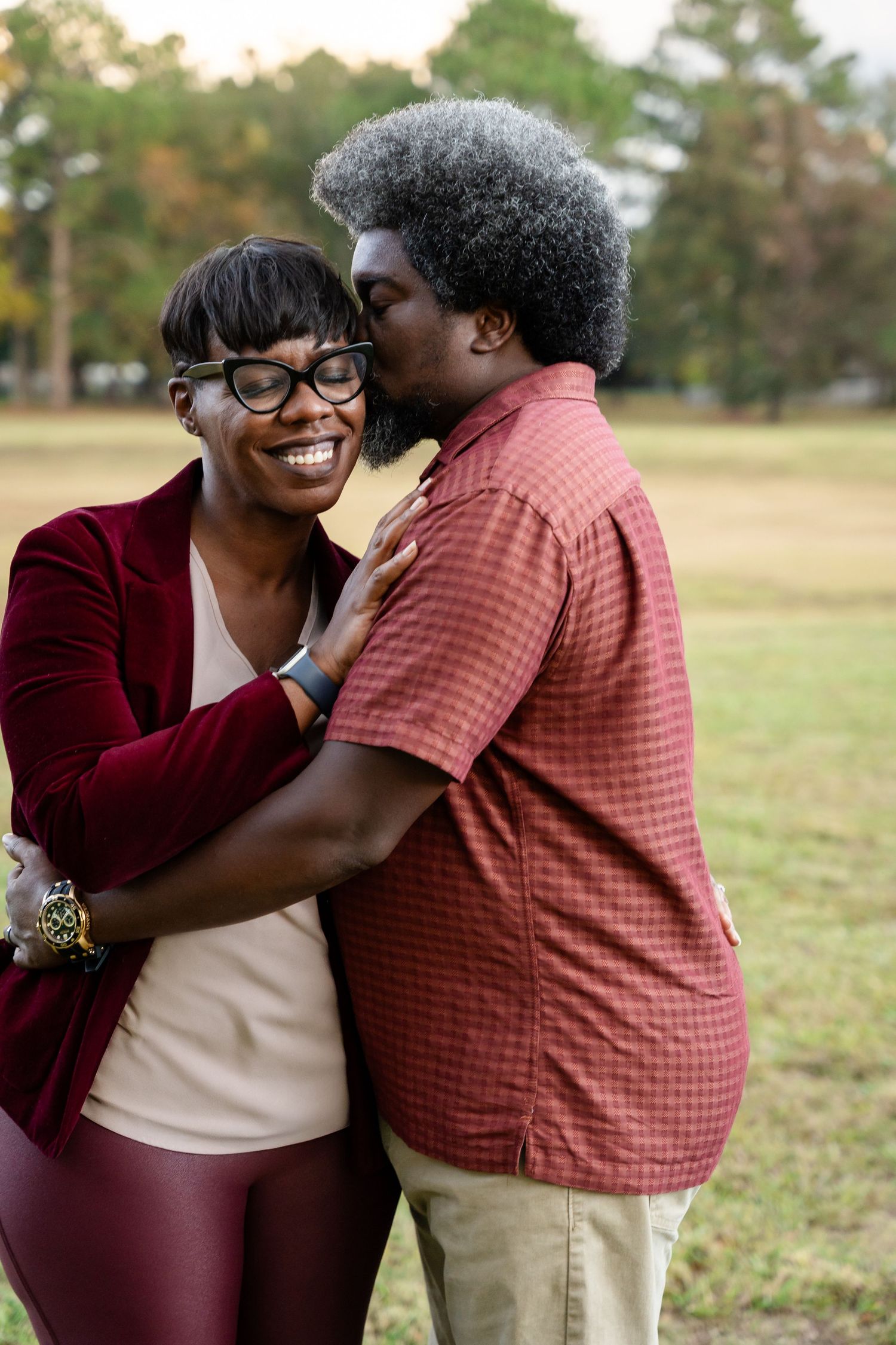 A warm embrace shared between two people wearing burgundy and coral colored clothing in a sunny outdoor setting.
