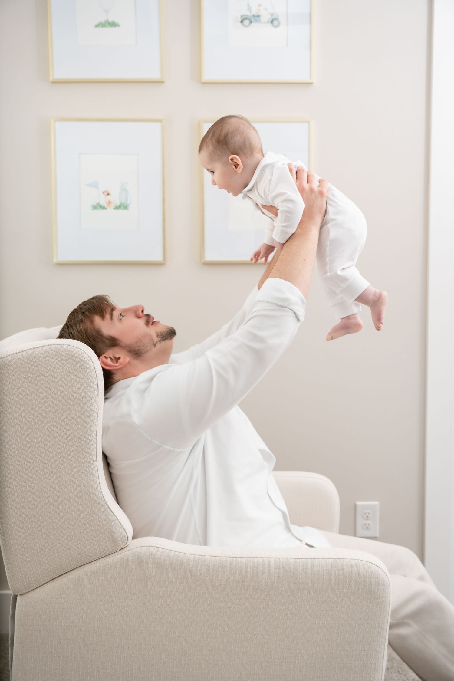 Playful moment in a nursery as baby is lifted high in the air above an armchair.