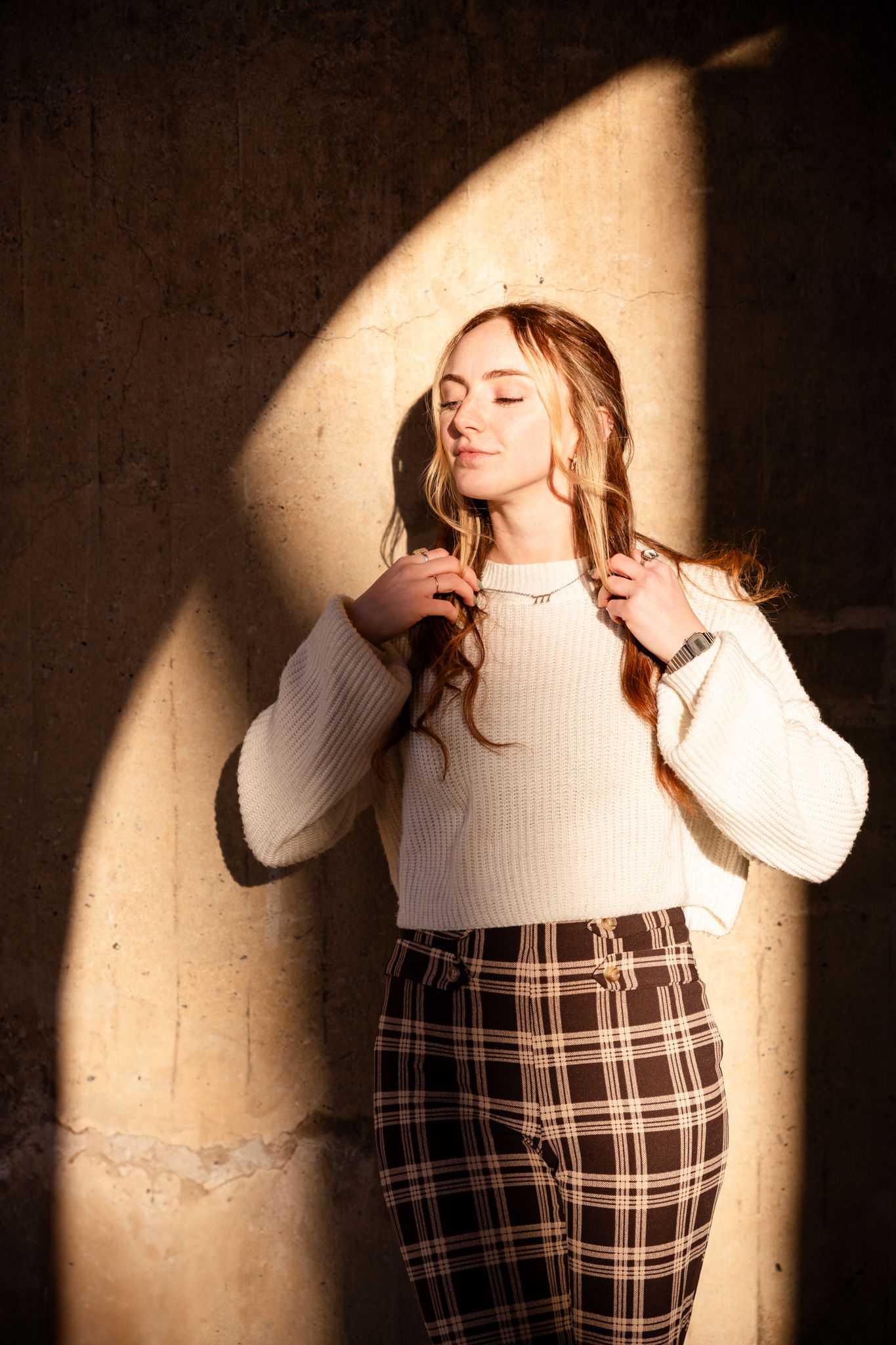 Dramatic lighting creates shadows in artistic portrait series against textured wall.