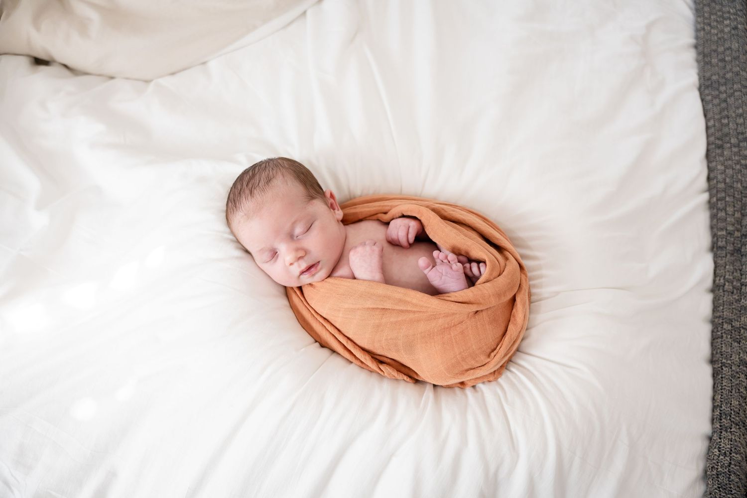Peaceful newborn photography with baby wrapped in peach-colored fabric on white bedding.