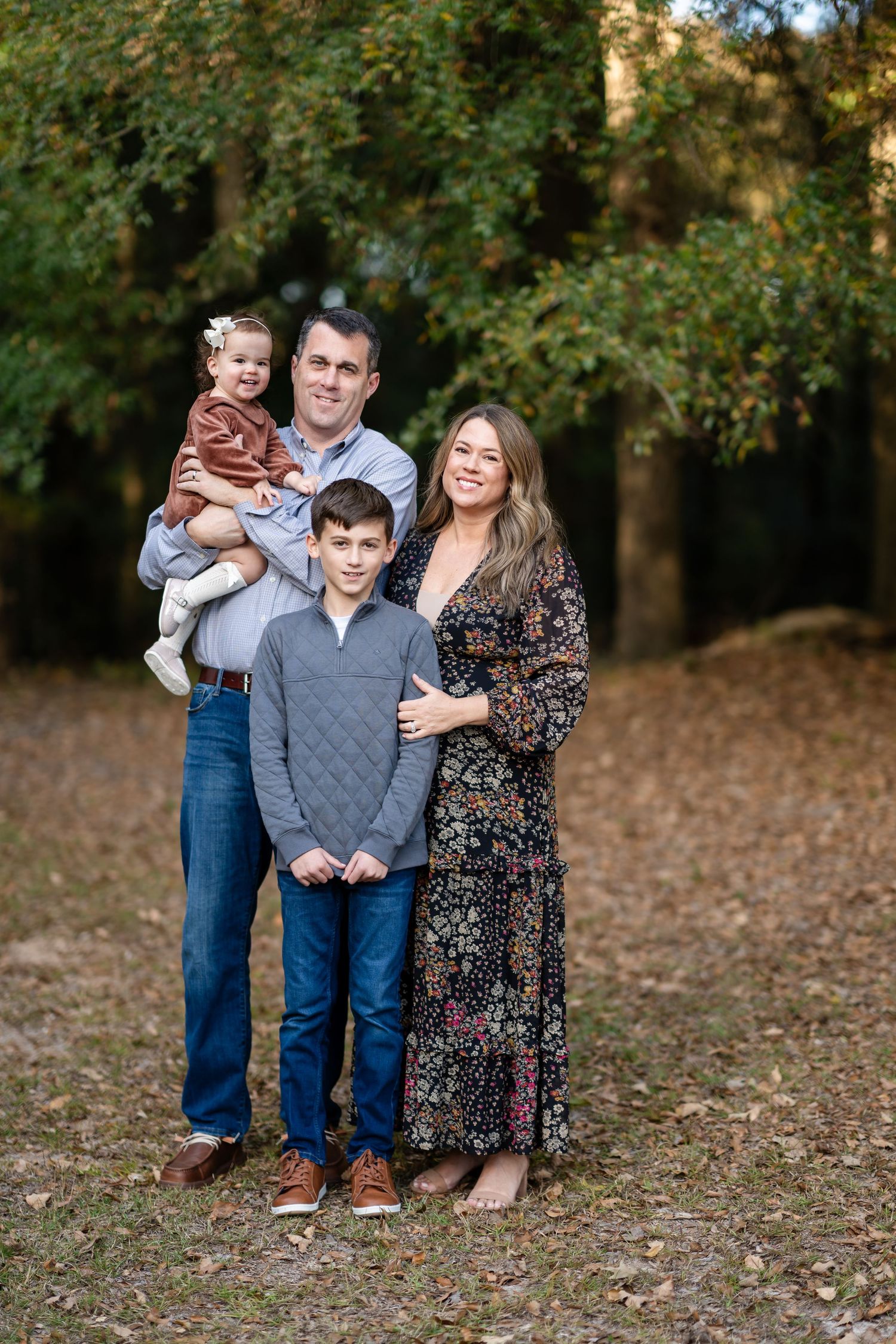 Family poses together on fallen autumn leaves in a park setting wearing coordinated casual outfits.