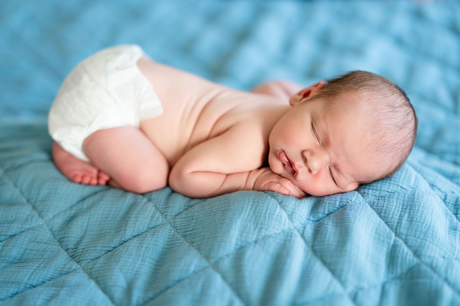 Sleeping newborn on teal blanket in soft natural lighting.