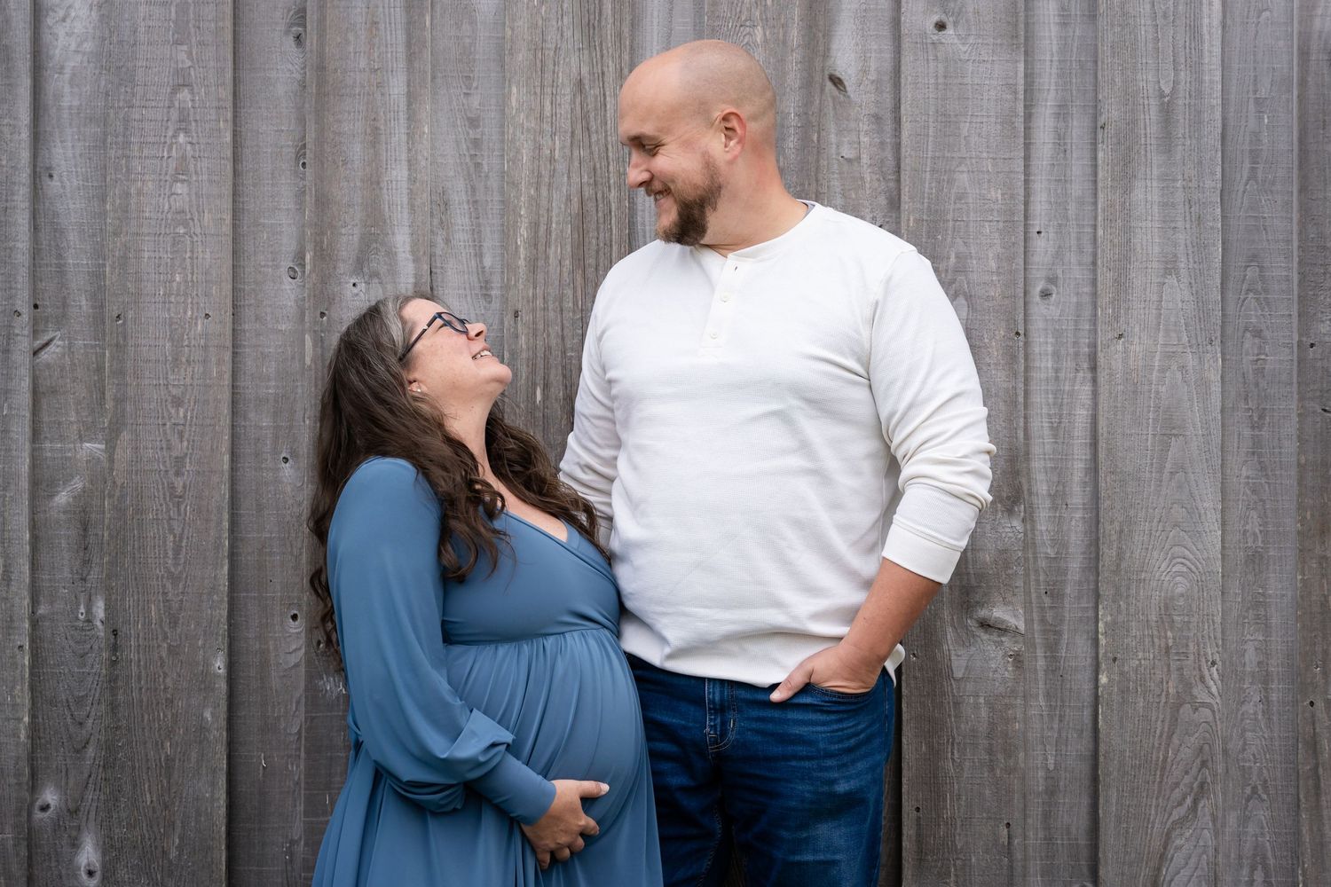 Couple takes maternity photos in front of rustic wooden wall showing close-up of embracing.