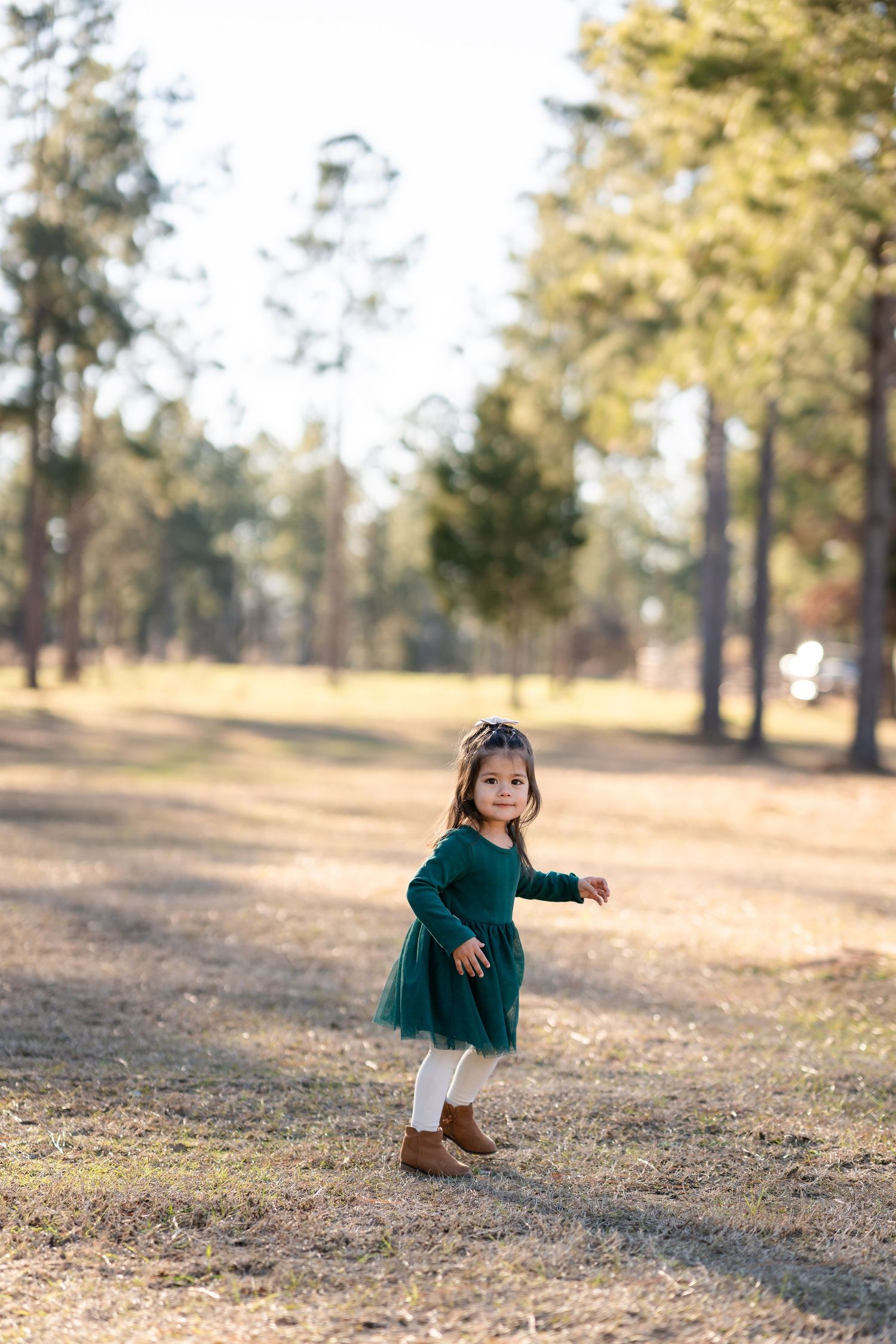 Child in green dress playing and running through a park during golden hour.