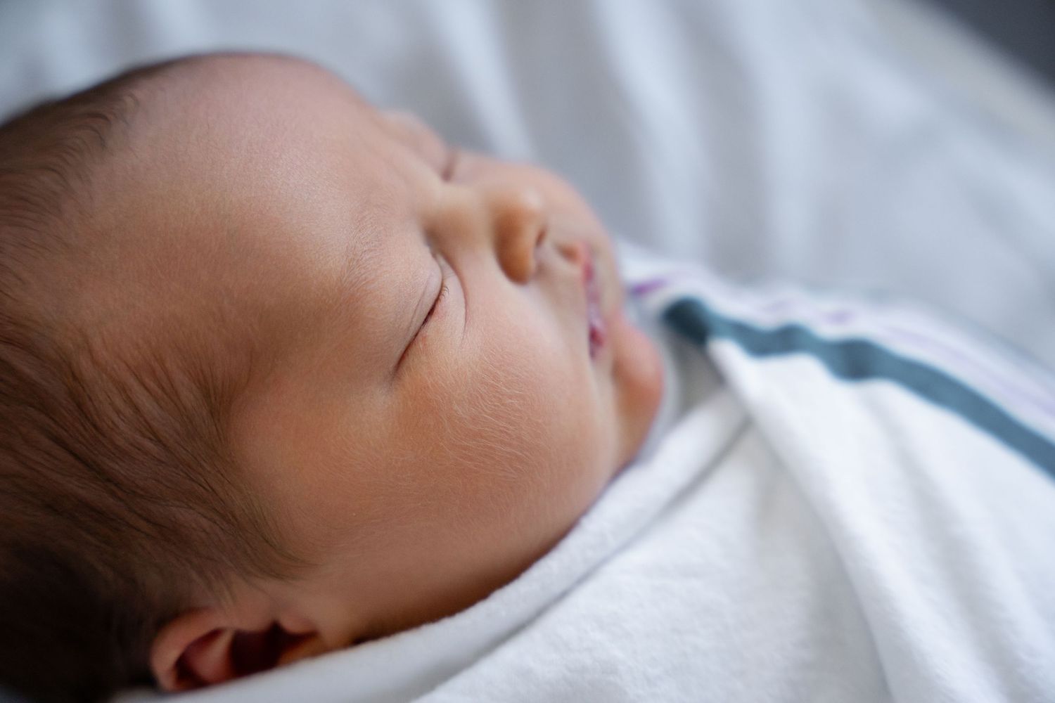 Sleeping newborn rests peacefully on white bedding.