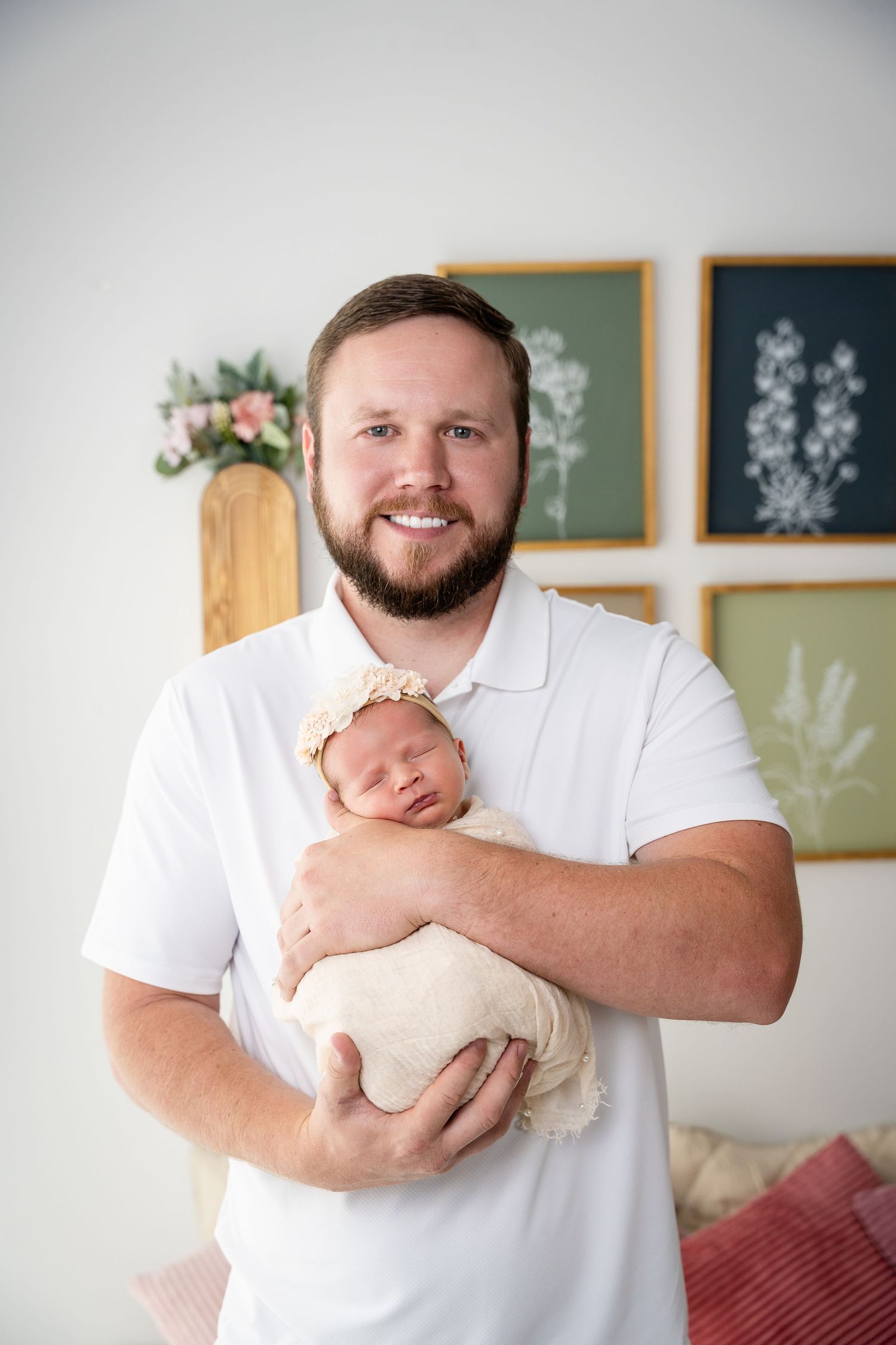 Indoor portrait session showing tender moments with newborn against botanical wall art.