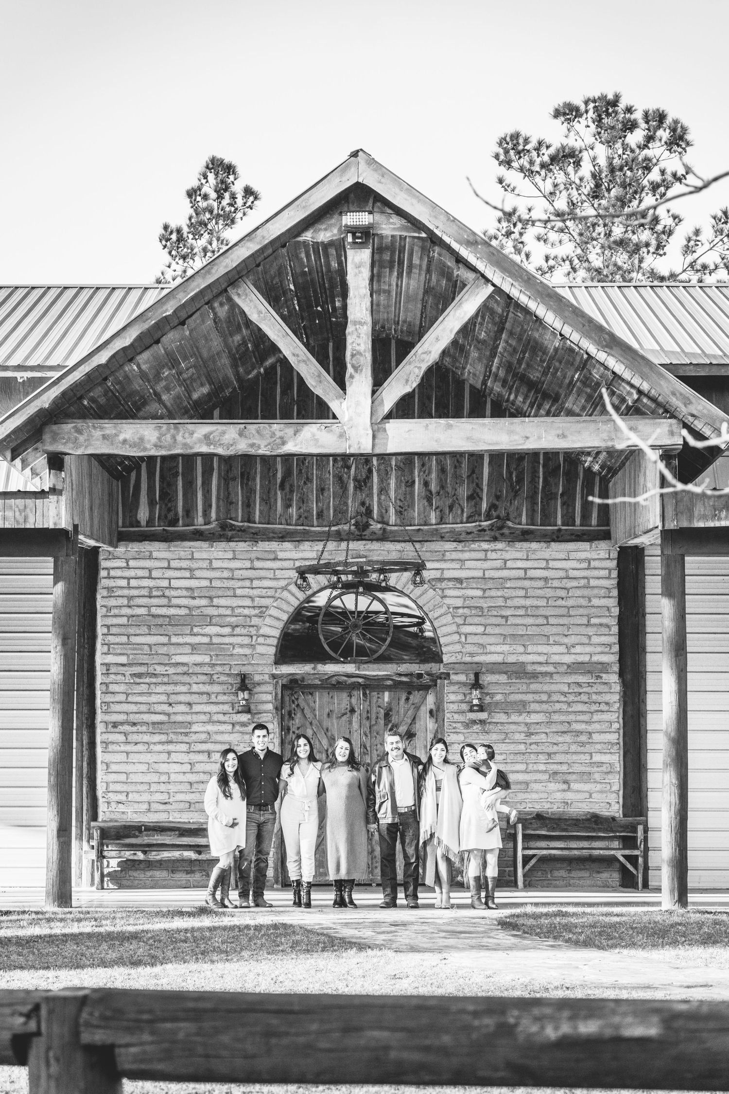 A nostalgic black and white photo of a group gathered on the porch of a rustic brick building.
