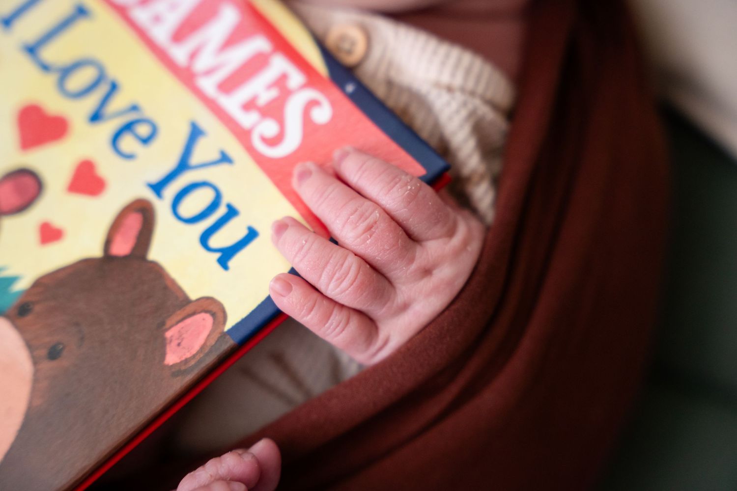Tiny baby hands resting on colorful storybook cover.