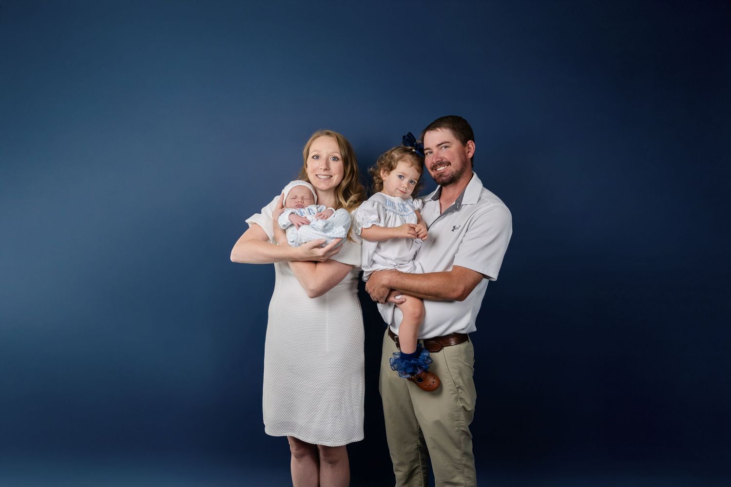 Family photo session with natural expressions against dark blue studio background.