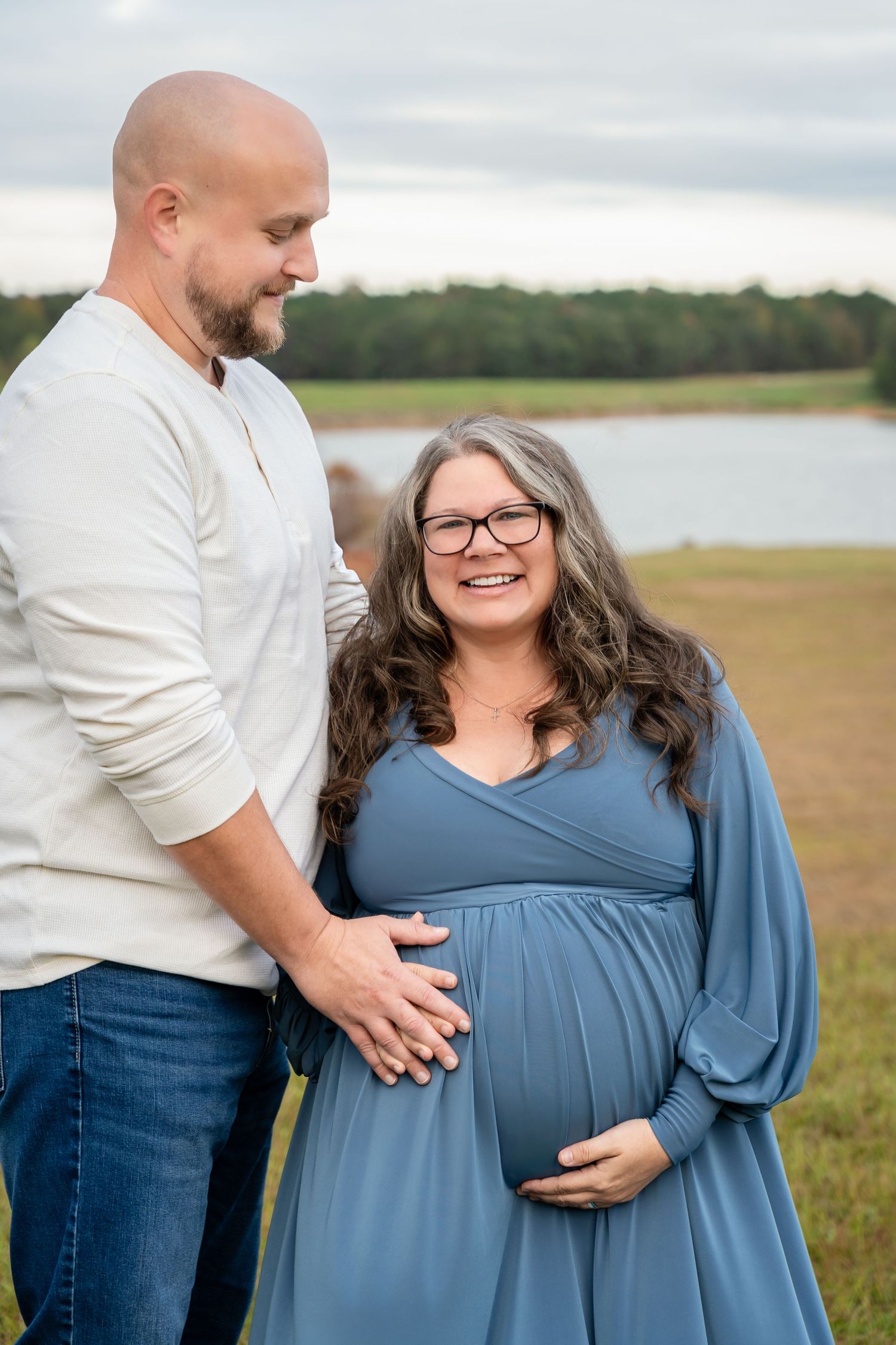 Maternity photoshoot in outdoor setting with lake and grass field in background.