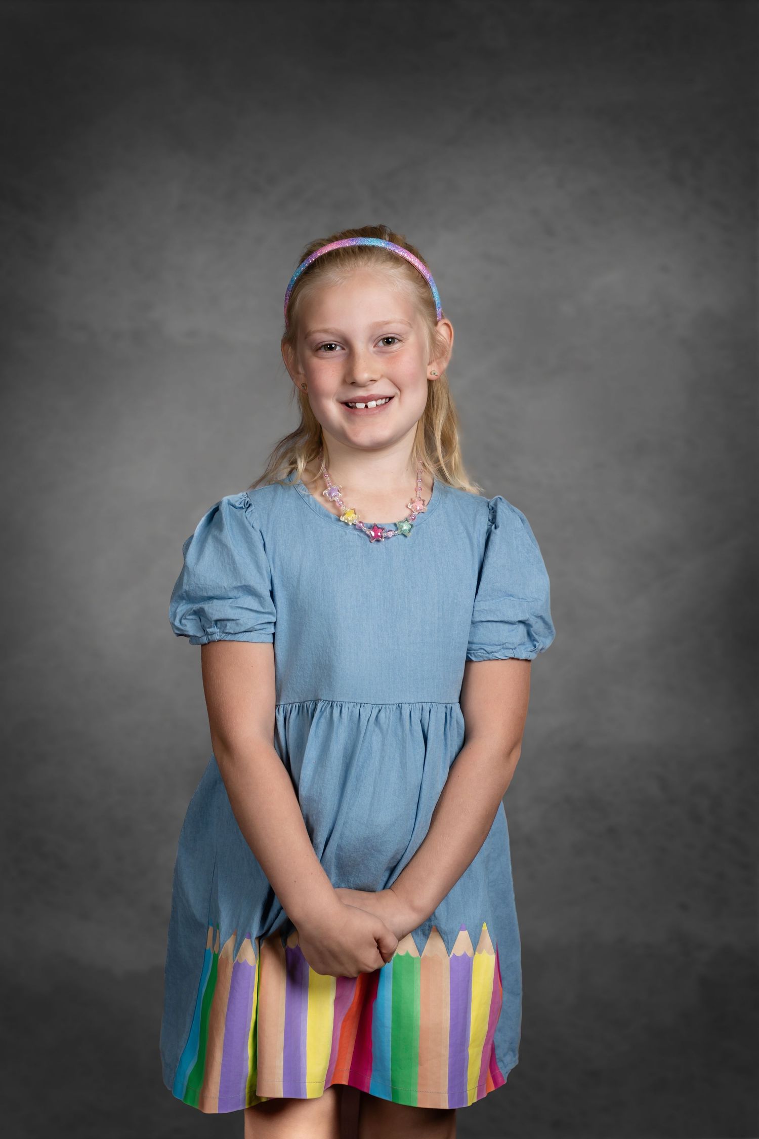 A light blue dress with colorful pencil-shaped stripes along the hem stands out against a gray studio backdrop.