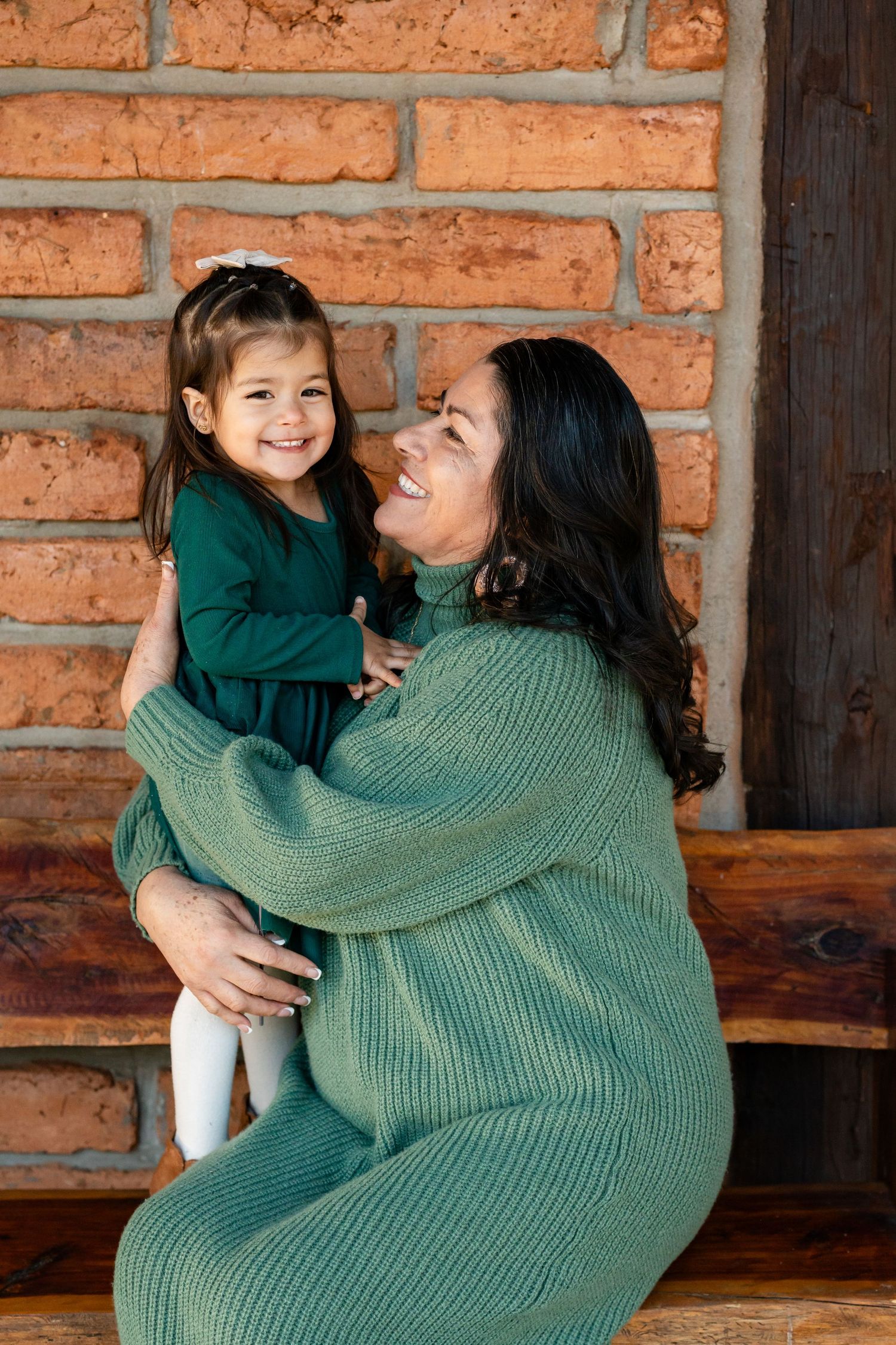 A joyful moment shared between two people wearing matching green sweaters against a brick wall.