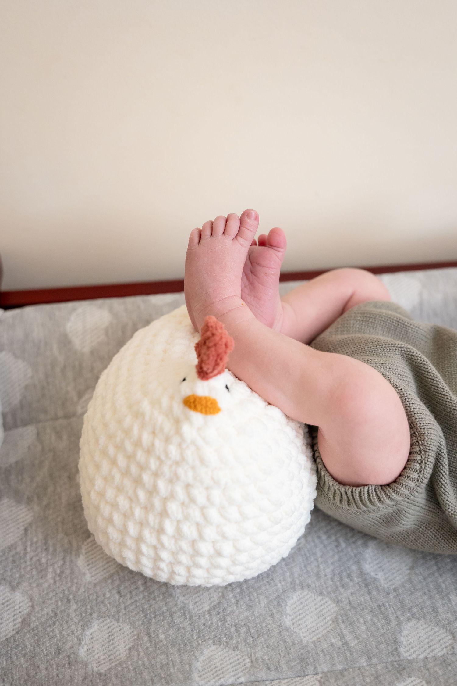 Tiny baby feet resting on a white crocheted snowman pillow with an orange carrot nose and red heart.