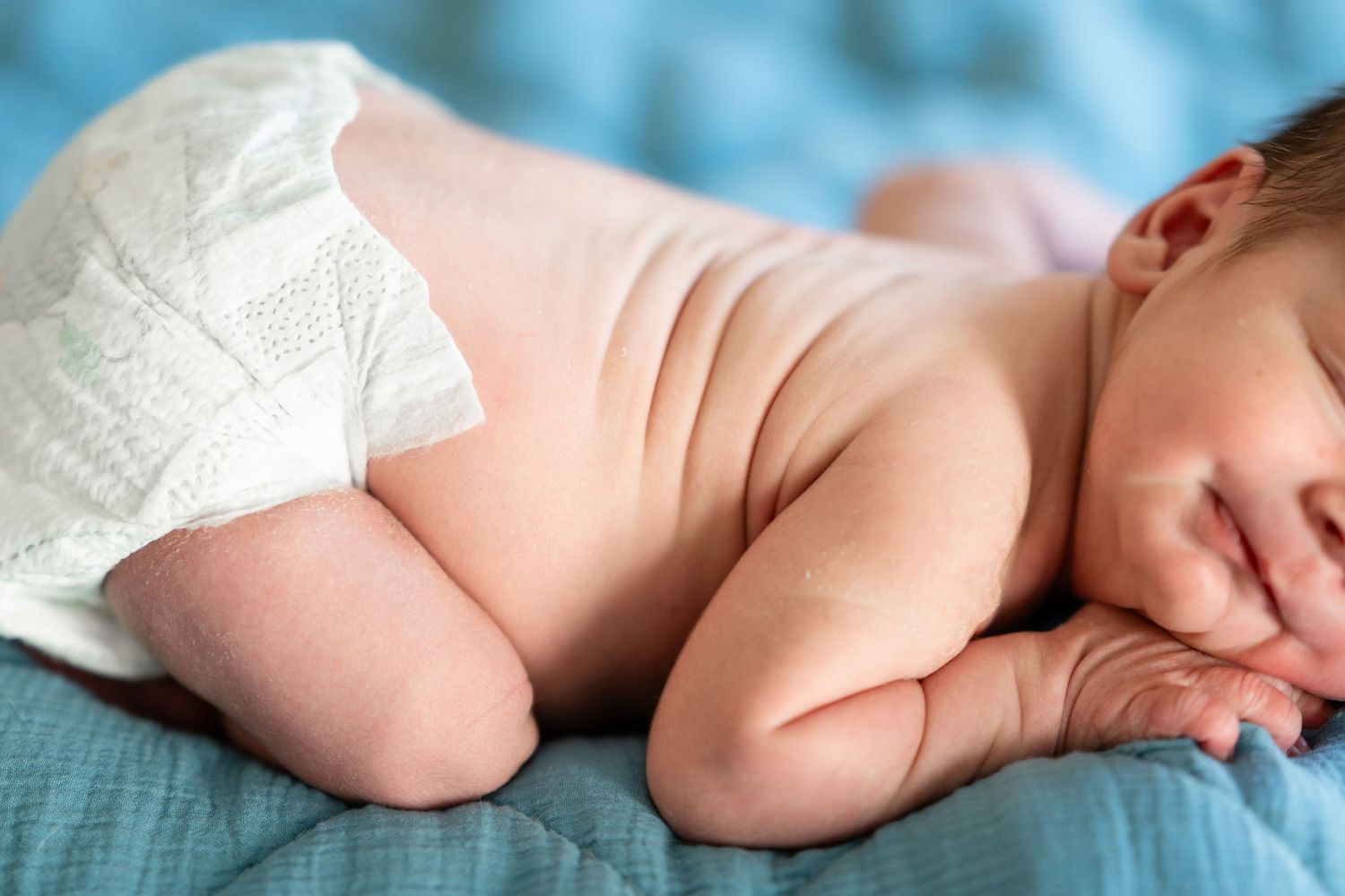 Newborn baby sleeping peacefully on blue bedding in soft focus.
