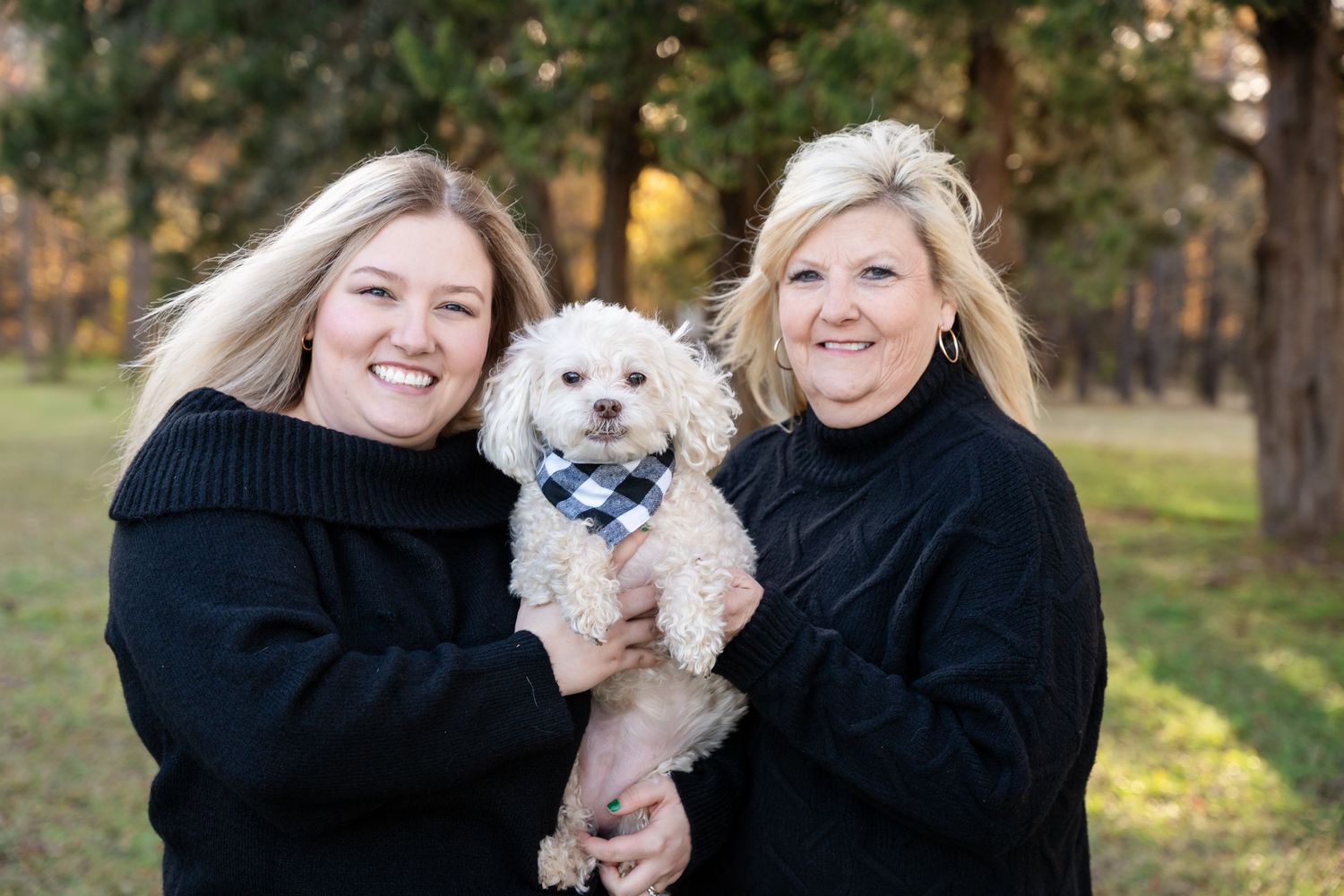 Family members in black sweaters pose with small white dog.