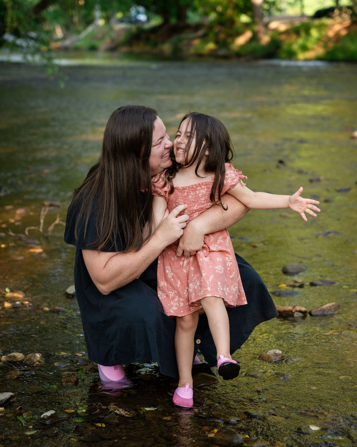 A tender outdoor moment near a stream with fall foliage in gentle natural lighting.