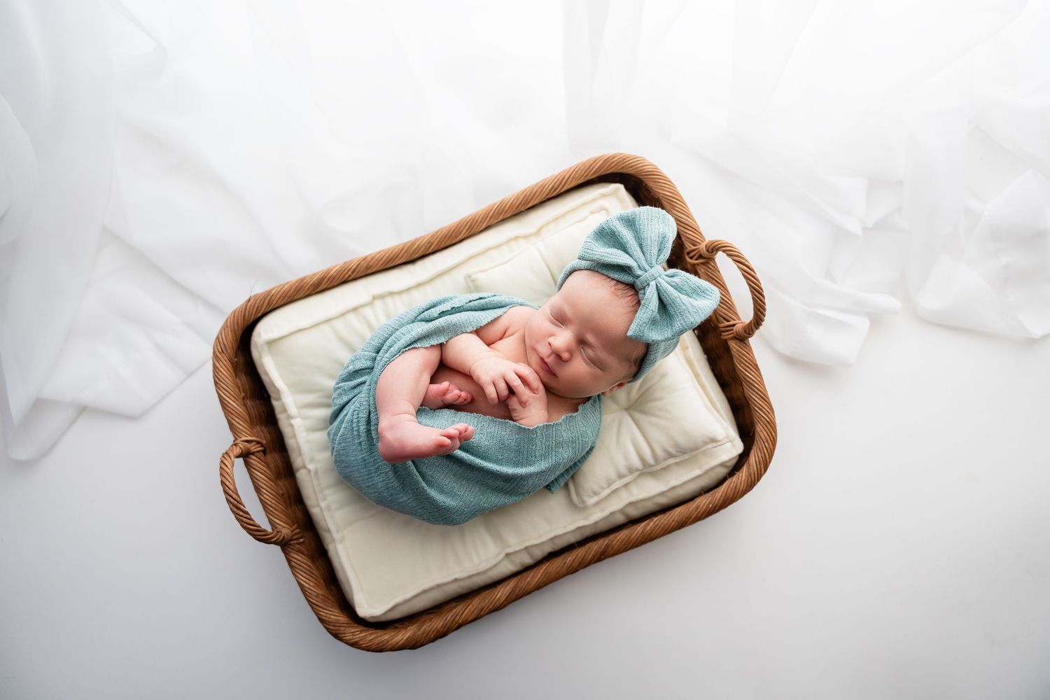 Newborn in blue outfit lying peacefully in wooden tray with white bedding.