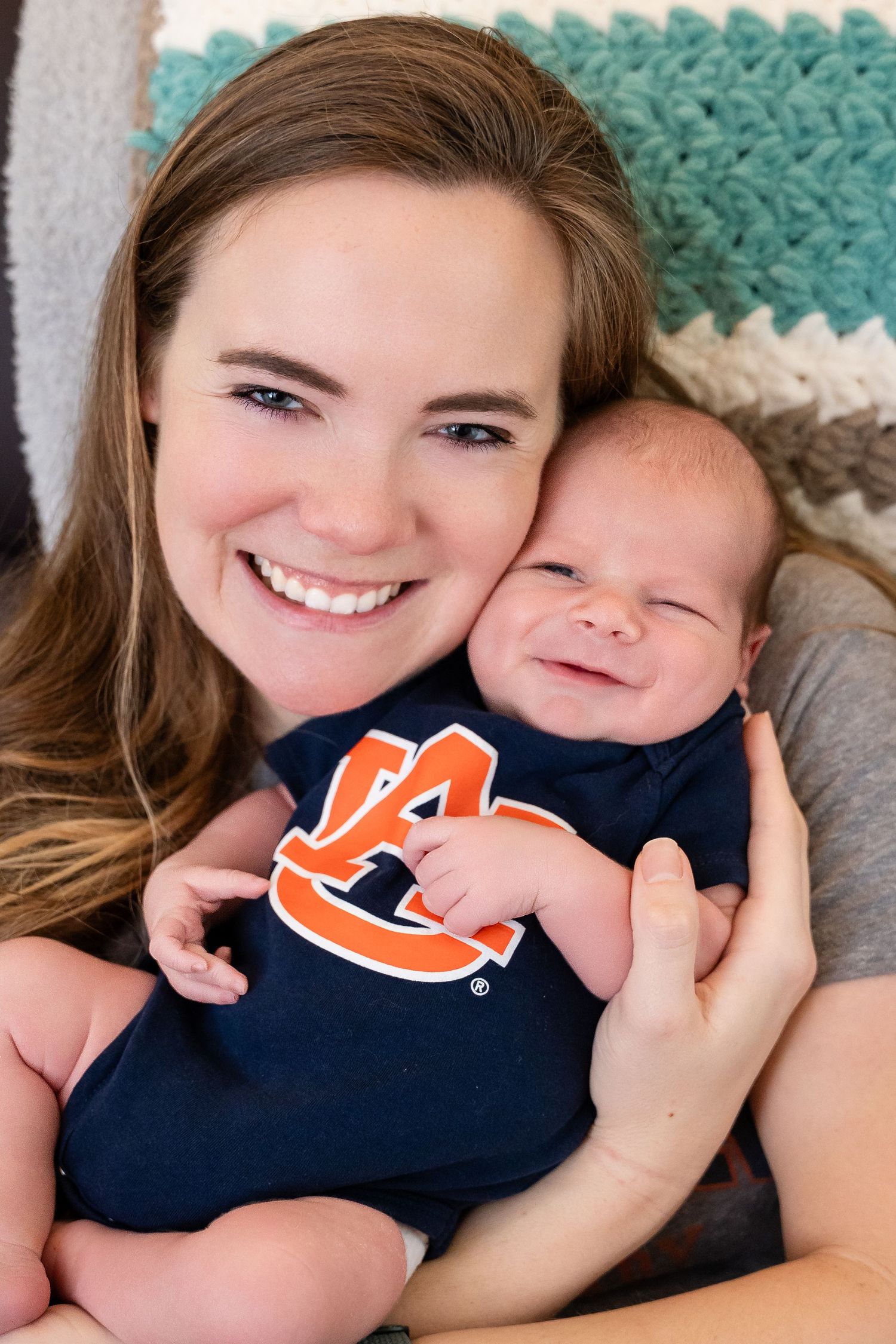 Baby wearing navy Auburn University onesie poses for newborn photo with loved one.