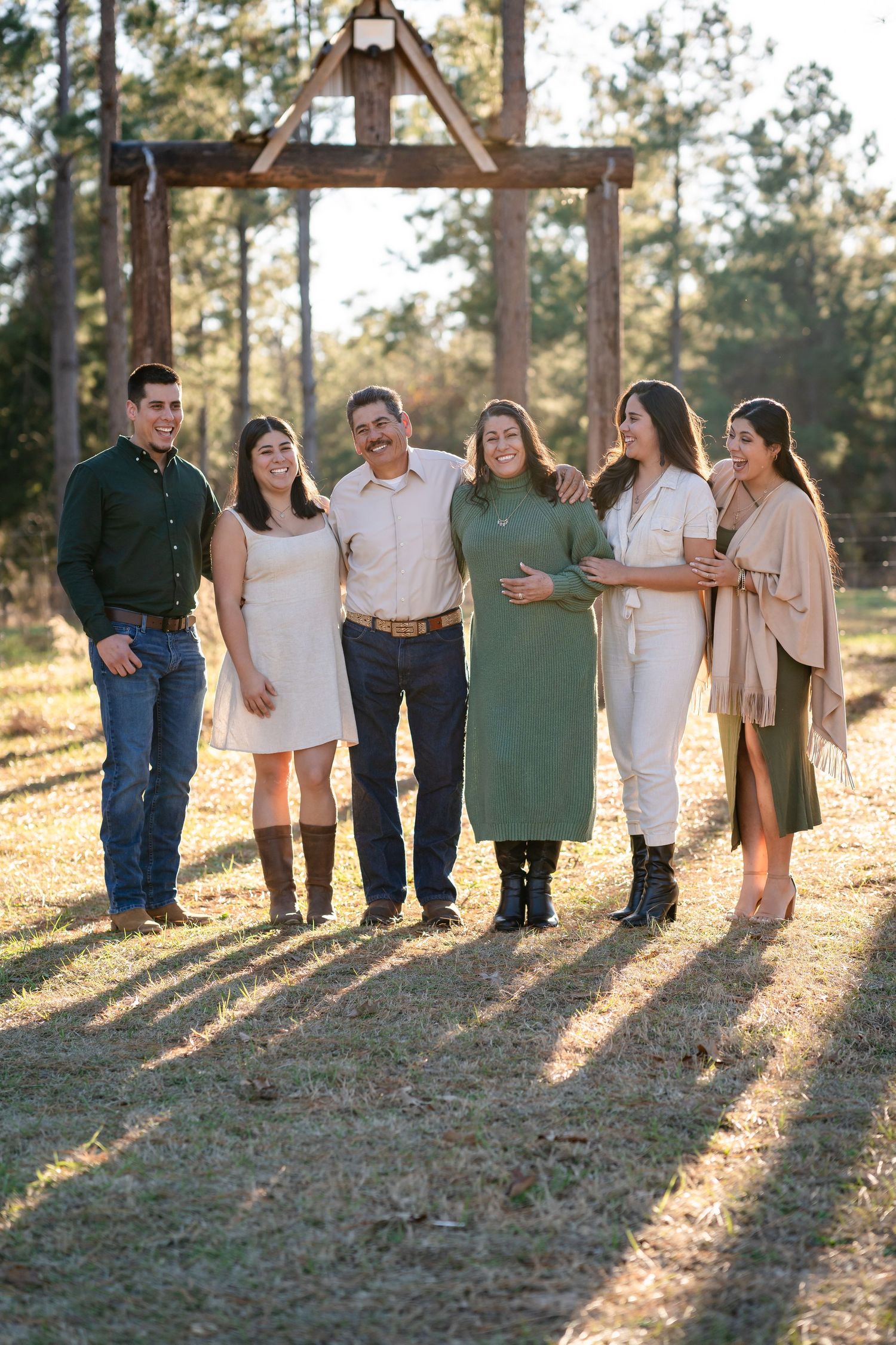 Extended family poses together in casual attire under pine trees with beautiful backlighting.