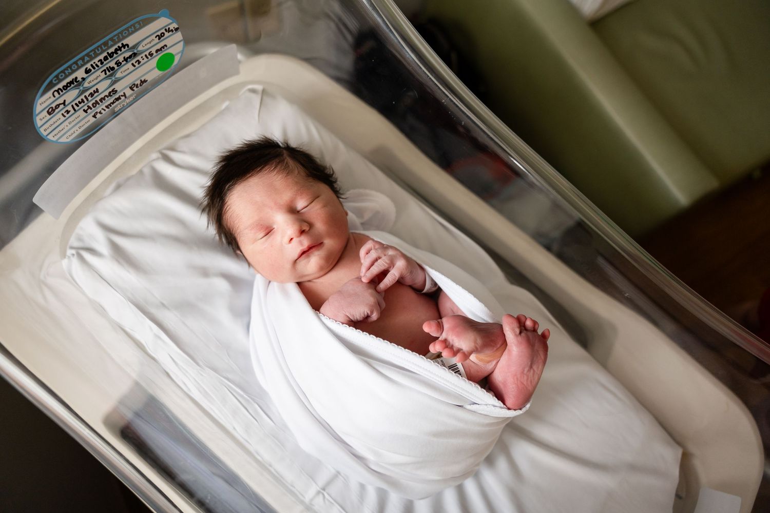 Close-up details of a sleeping newborn baby in a hospital bassinet.