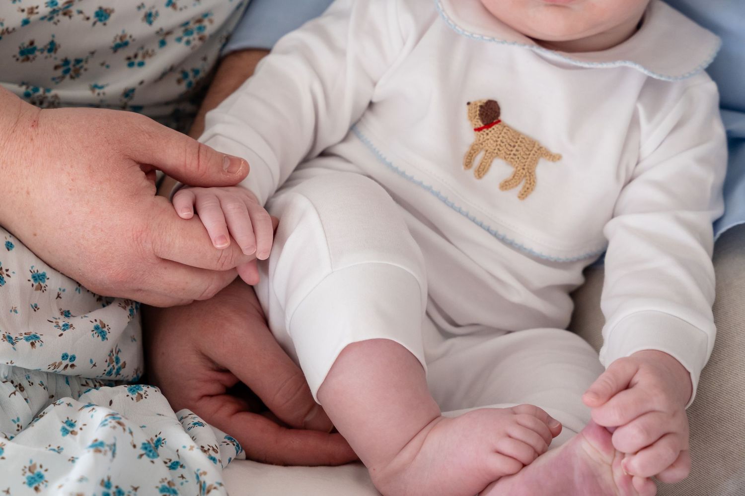 Close-up details of baby wearing white onesie on soft bedding.