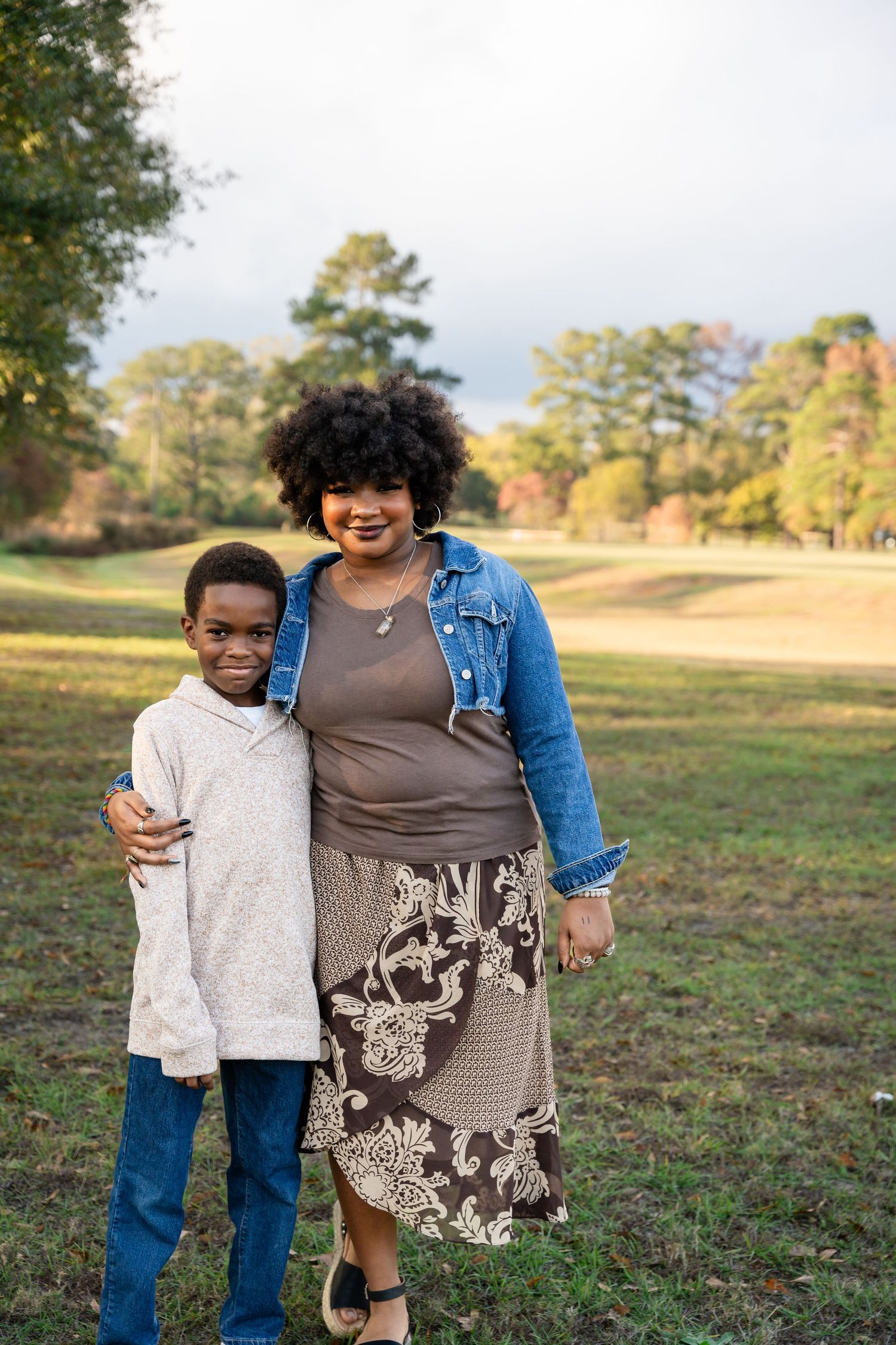 Mother and child sharing a warm embrace while standing in a grassy field during golden hour.