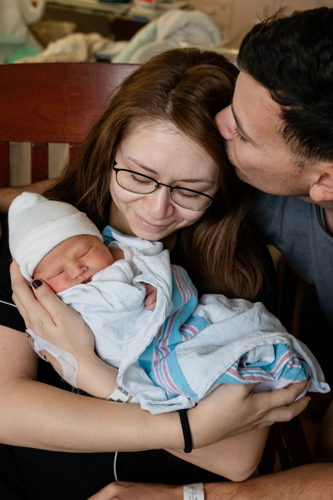 Loving parents cradle their newborn baby wrapped in hospital blanket.