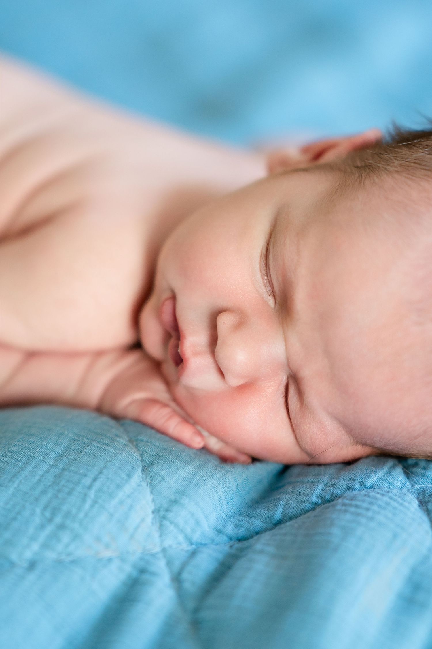 Peaceful sleeping baby resting on light blue bedding with natural lighting.