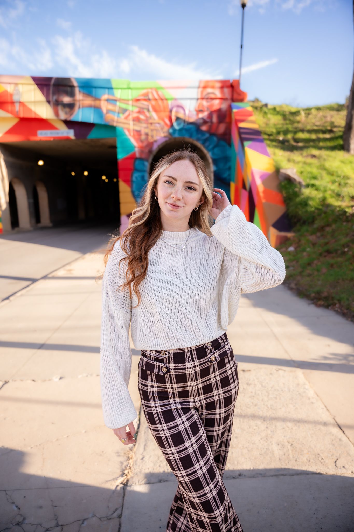 Fashion portrait series against colorful street art mural wearing white sweater and plaid pants.