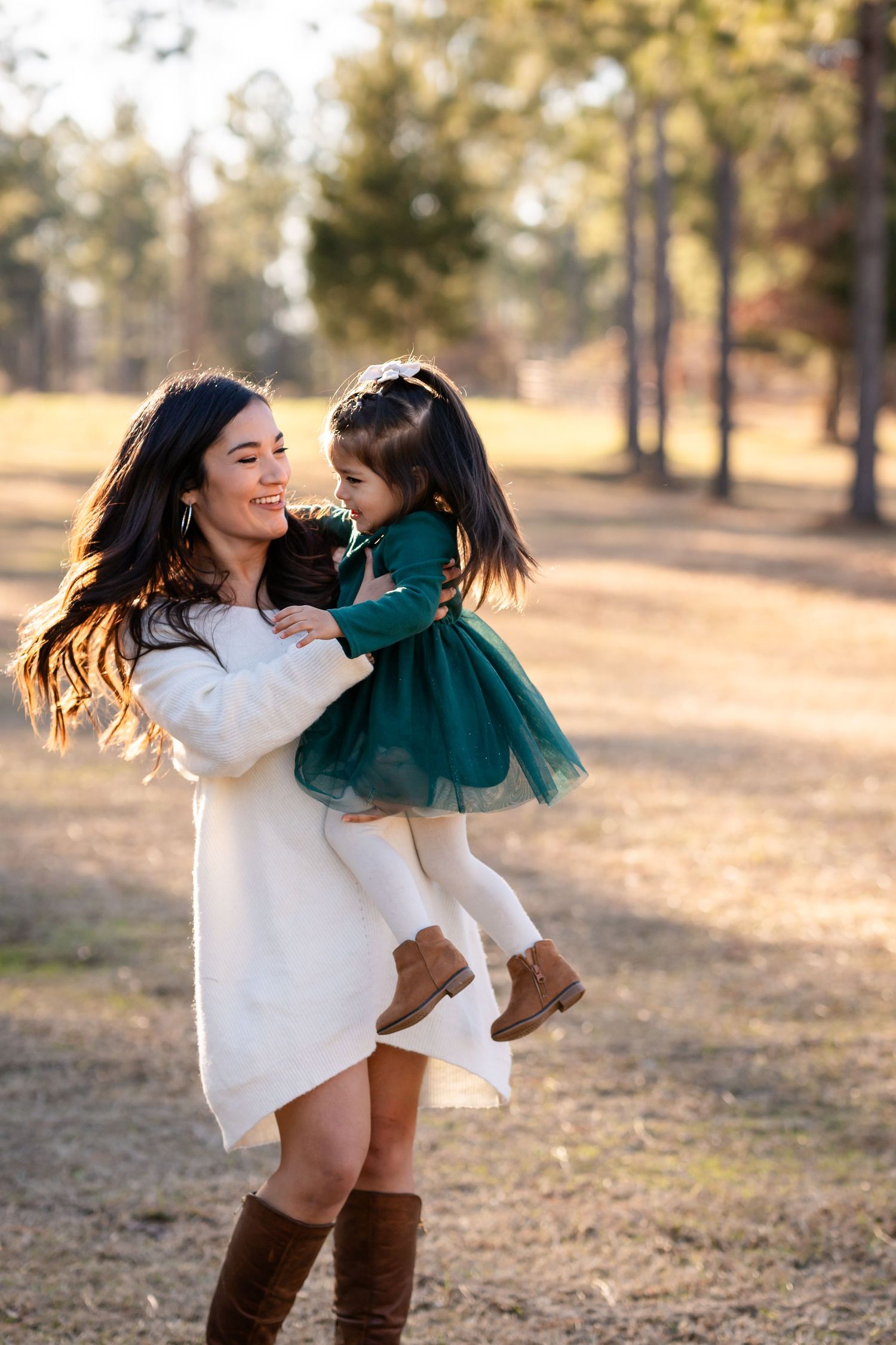 Two people in white and green dresses playing and dancing together in sunny forest setting.