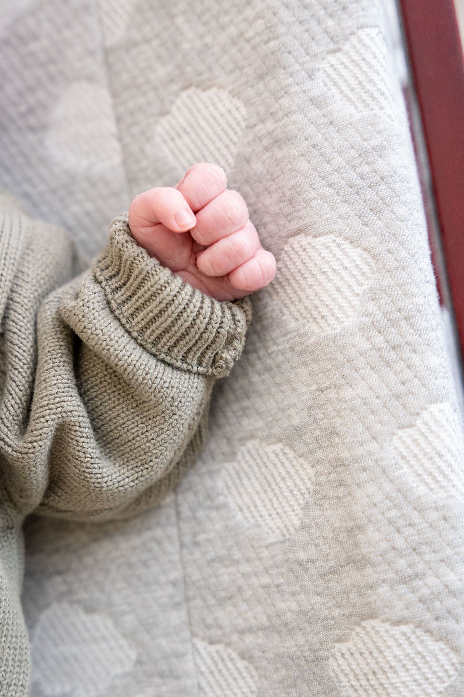 Close-up of tiny baby hand grasping gray knit sweater against patterned background.