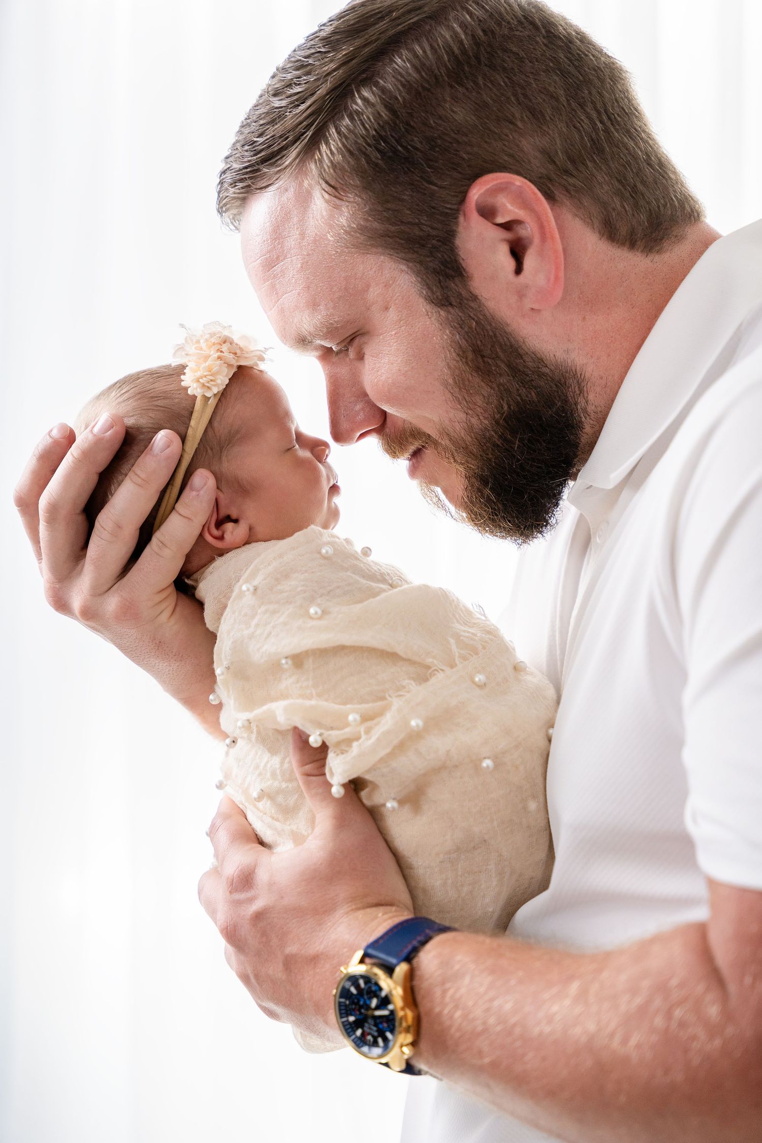 Intimate newborn photography session showing gentle embraces in white studio setting.