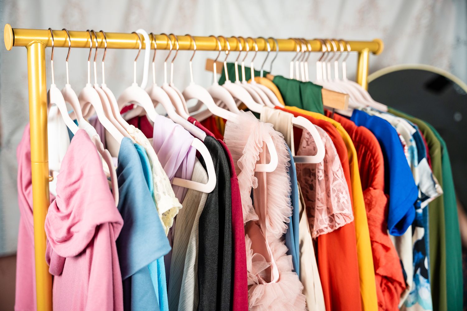 Colorful clothing hanging on a gold metal rack with pink, blue, and red garments.