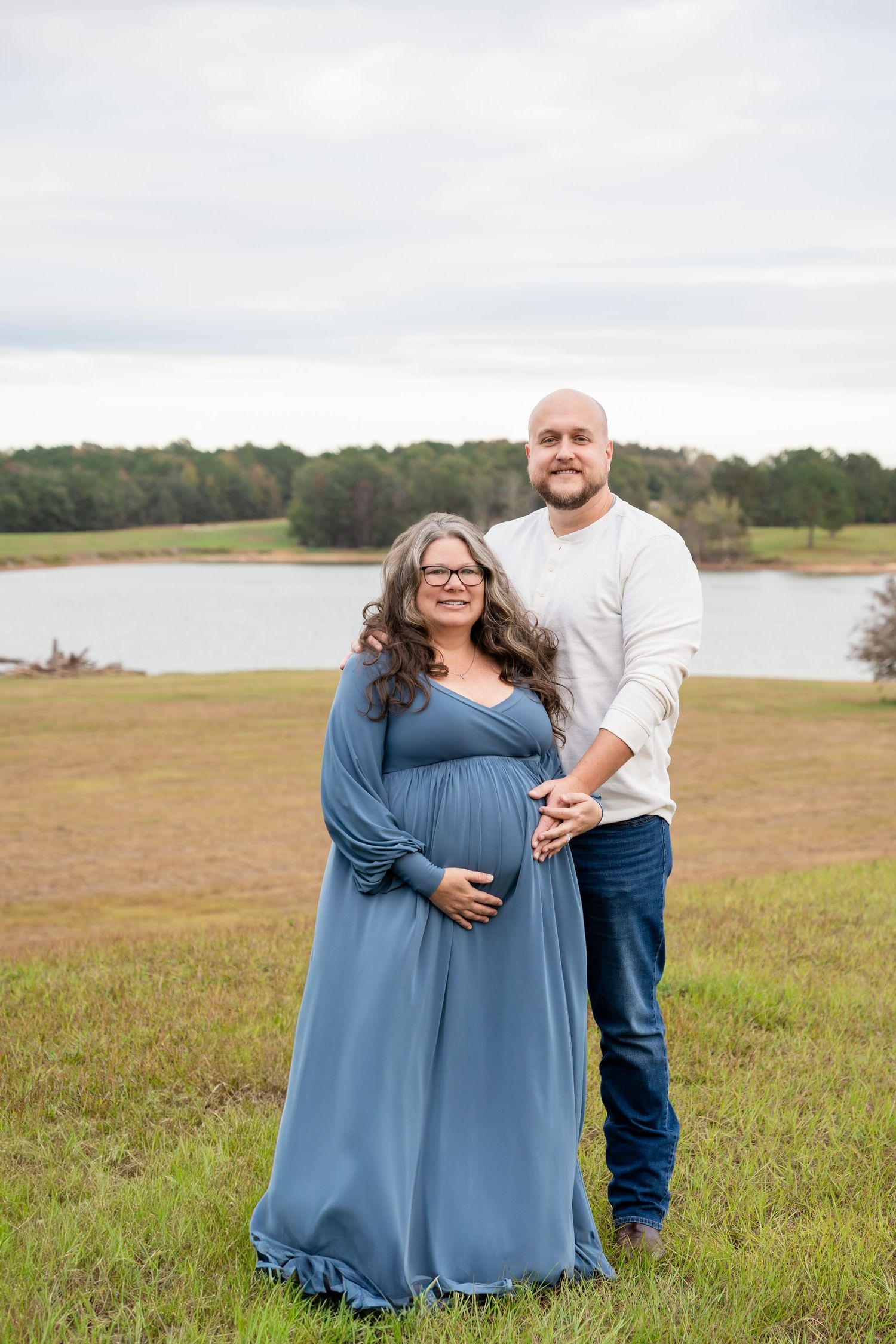 Couple embracing in casual outfits during outdoor photoshoot by lakeside landscape.