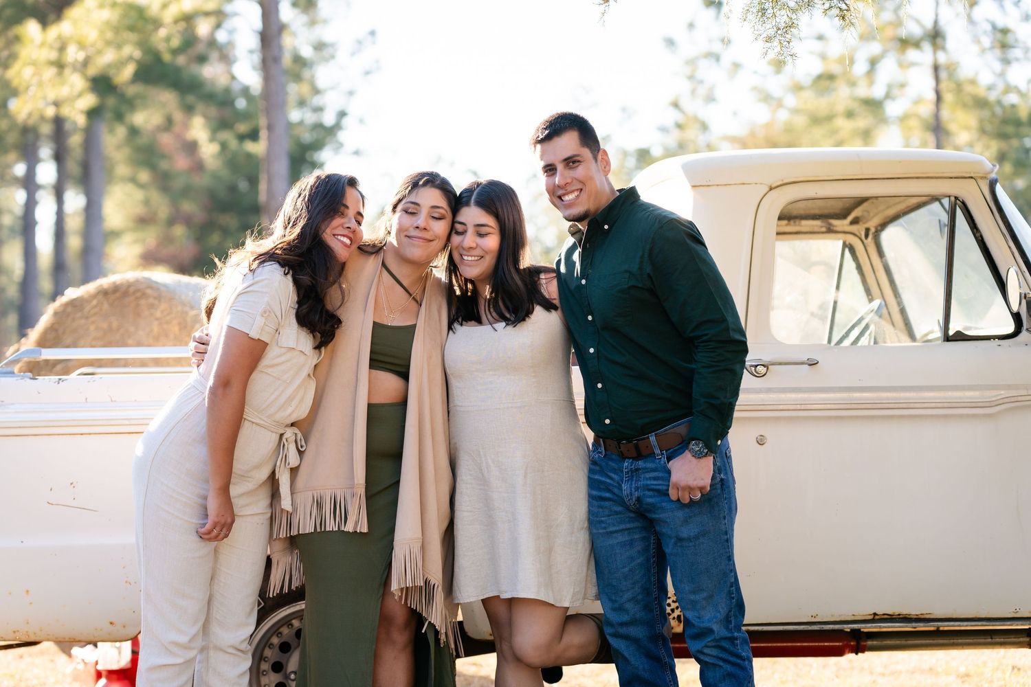 A group poses together outdoors next to a vintage car on a sunny day.