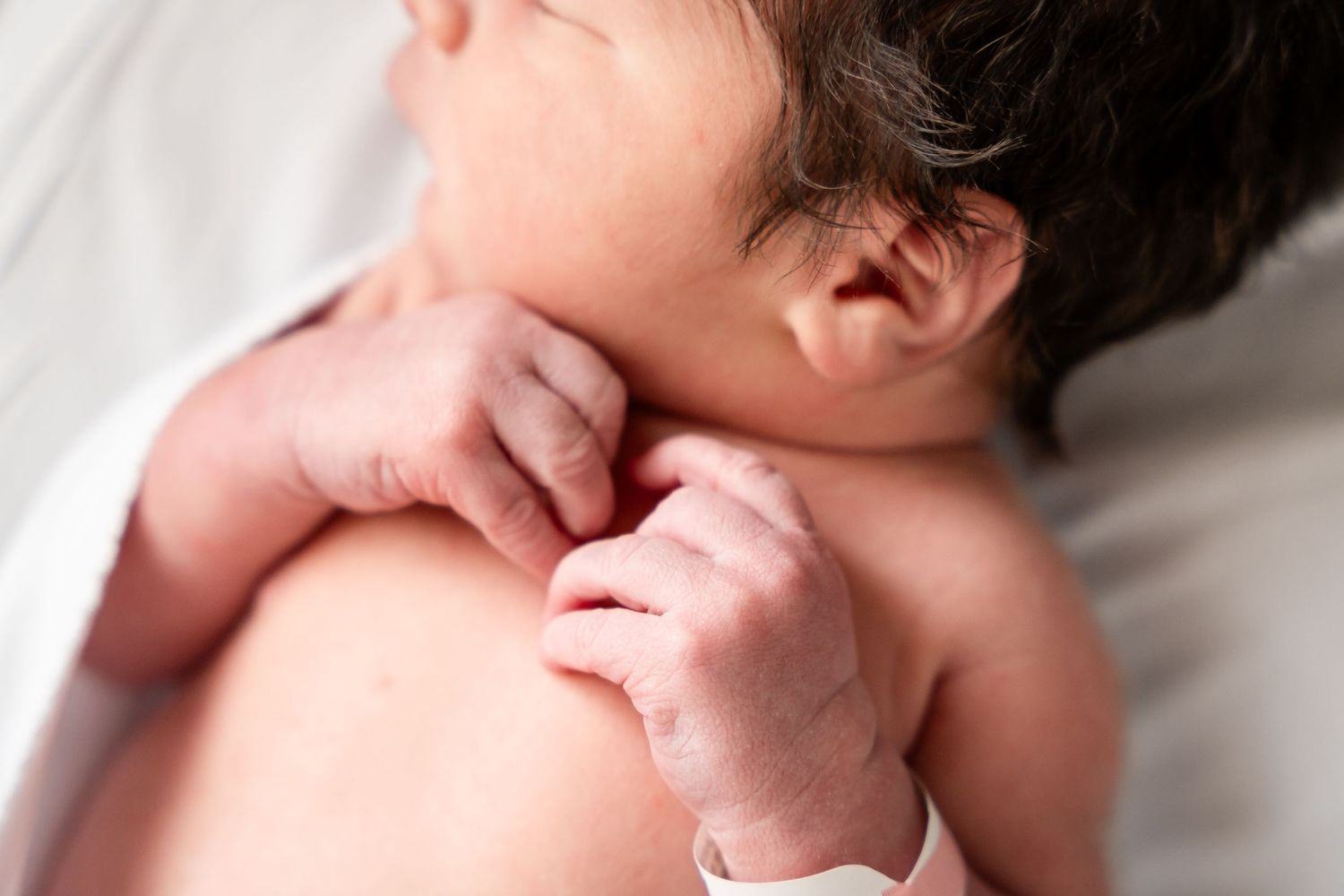 Newborn baby sleeping peacefully in white hospital bassinet.