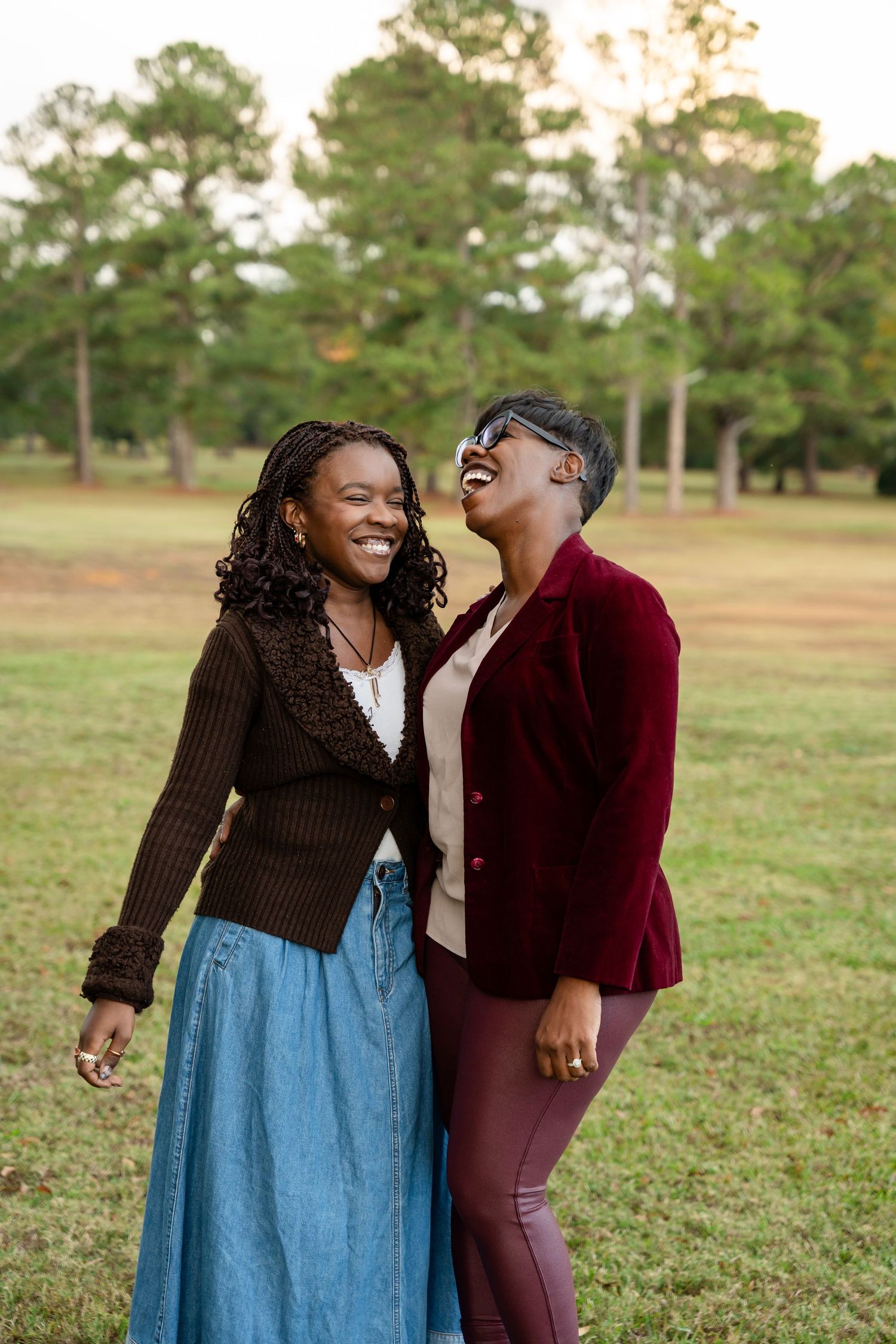Two people laughing together in a park during autumn with trees in the background.