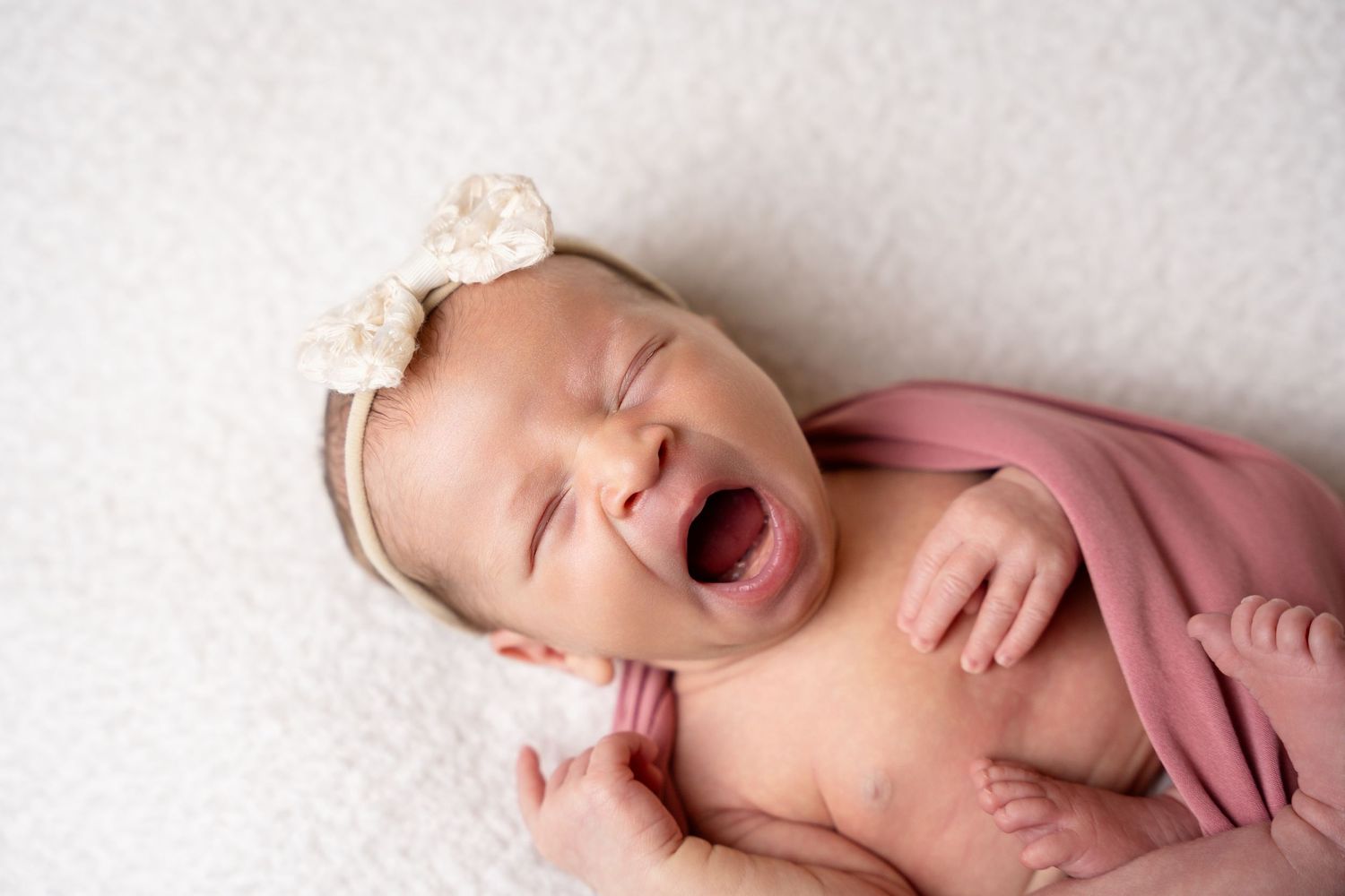 Sleeping newborn on white backdrop with pink fabric draping.