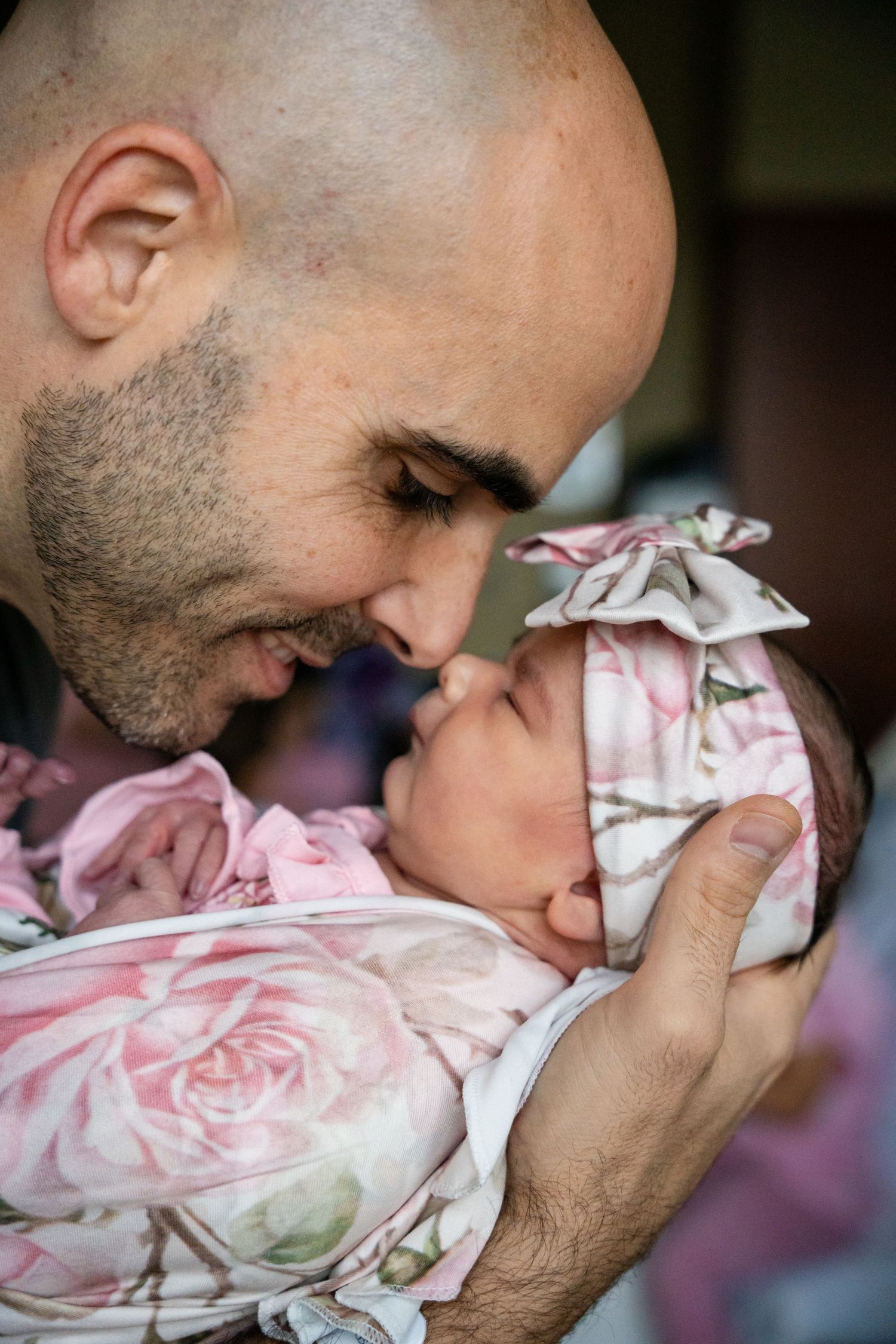 Tender moment captured of parent cradling newborn wrapped in floral fabric.