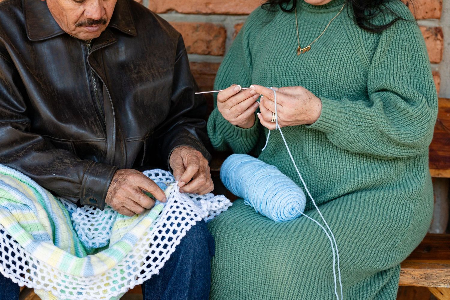 Close-up of hands working on a knitting project with blue yarn and colorful blanket.
