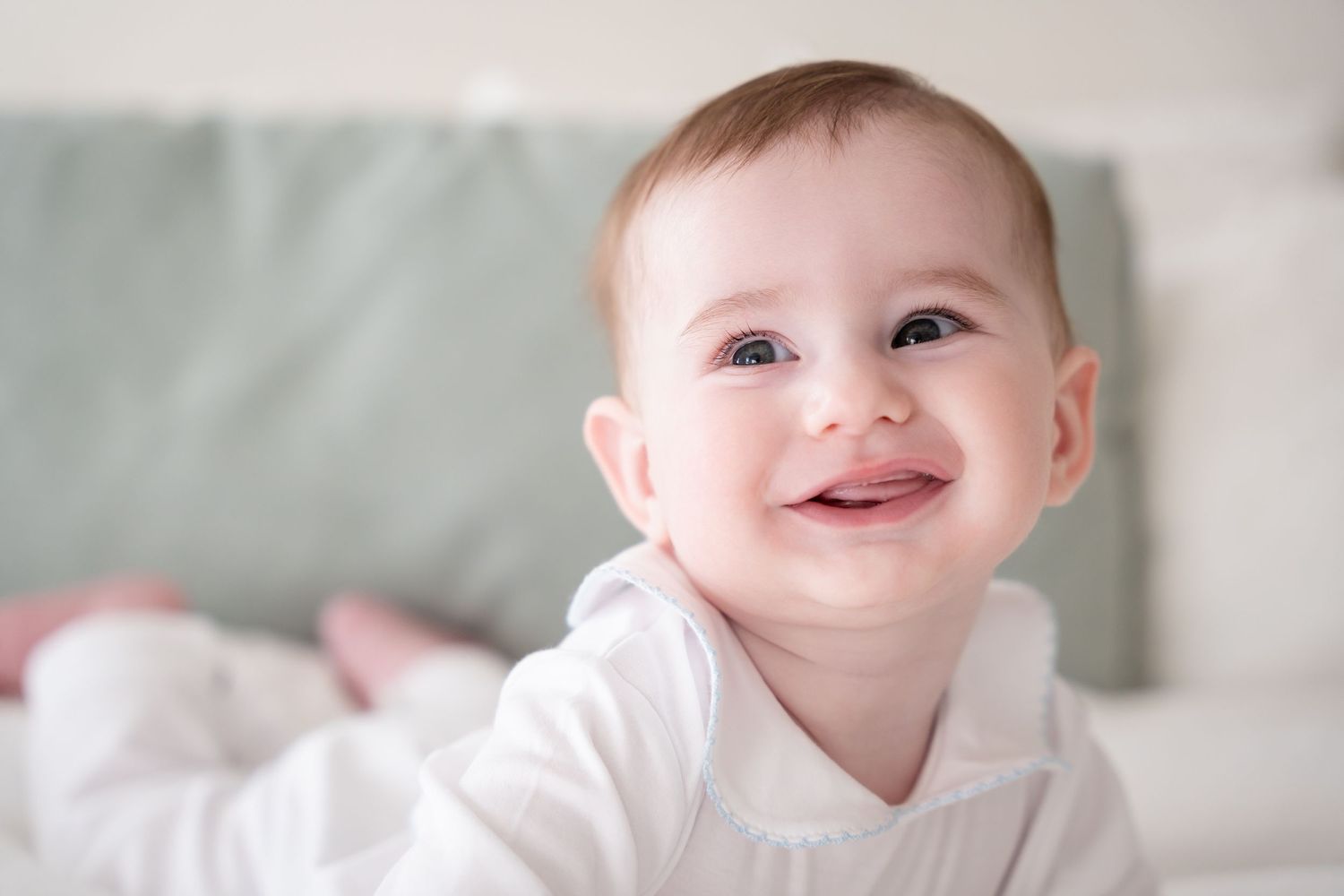 A baby in white clothing lying down and smiling brightly at the camera.