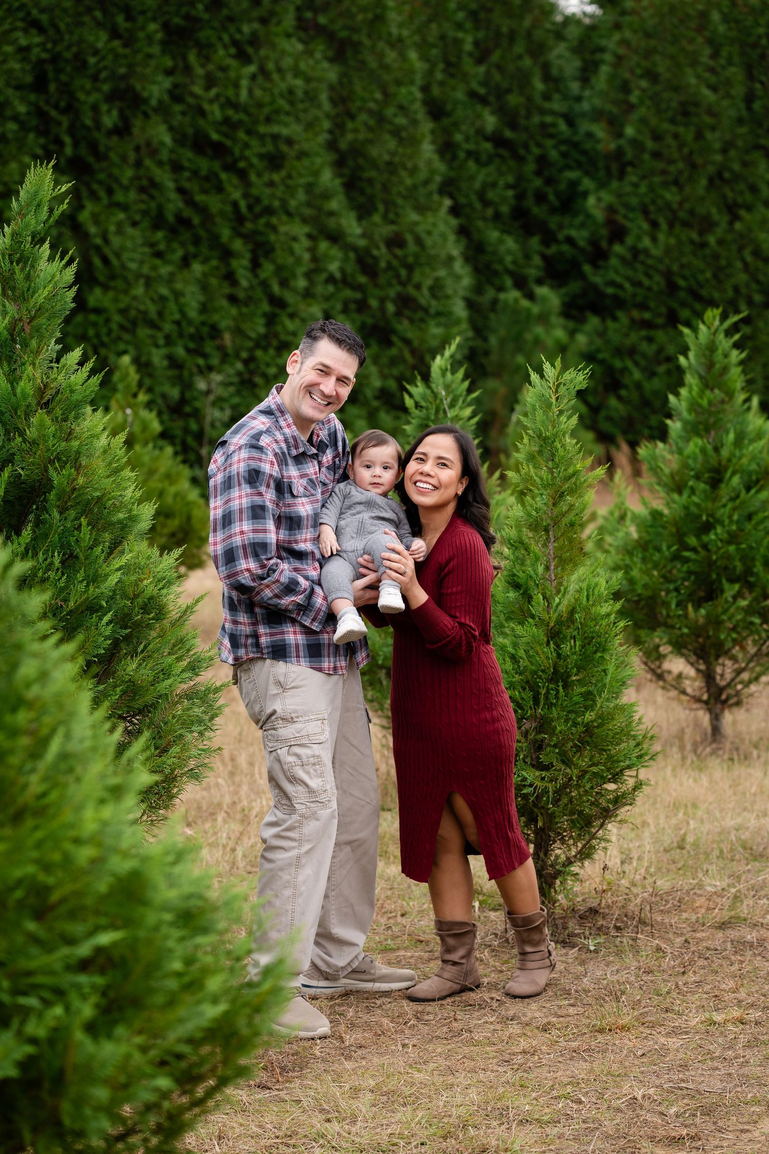 Family poses together among evergreen trees at a Christmas tree farm.