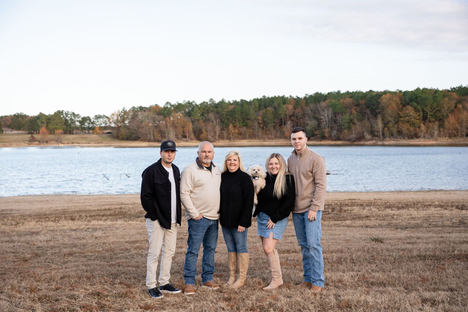 Family portrait session on beach with water and trees in background.