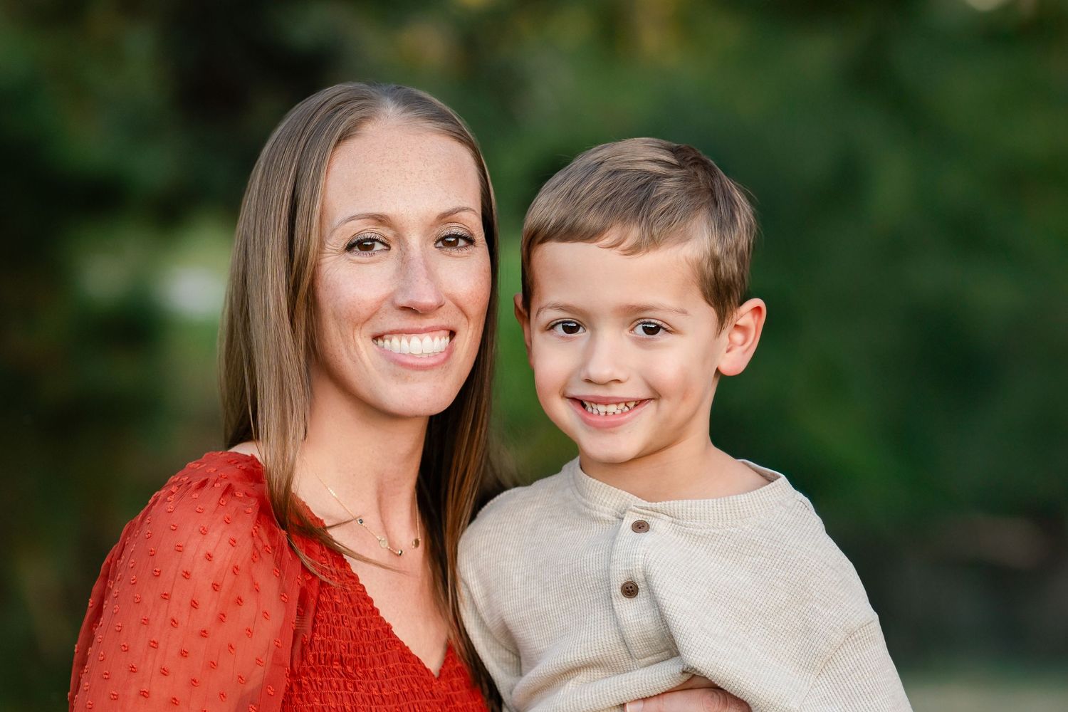 A close-up outdoor portrait with a red polka dot top and beige sweater against a blurred green background.