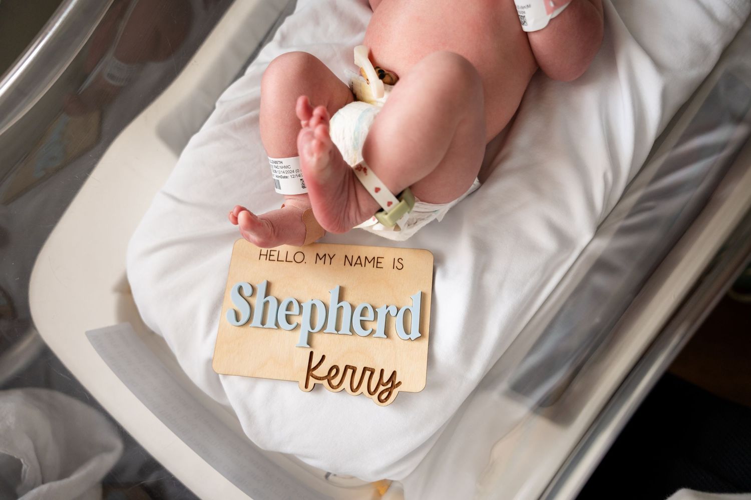 Hospital name tag reading 'Shepherd' visible in newborn's bassinet.
