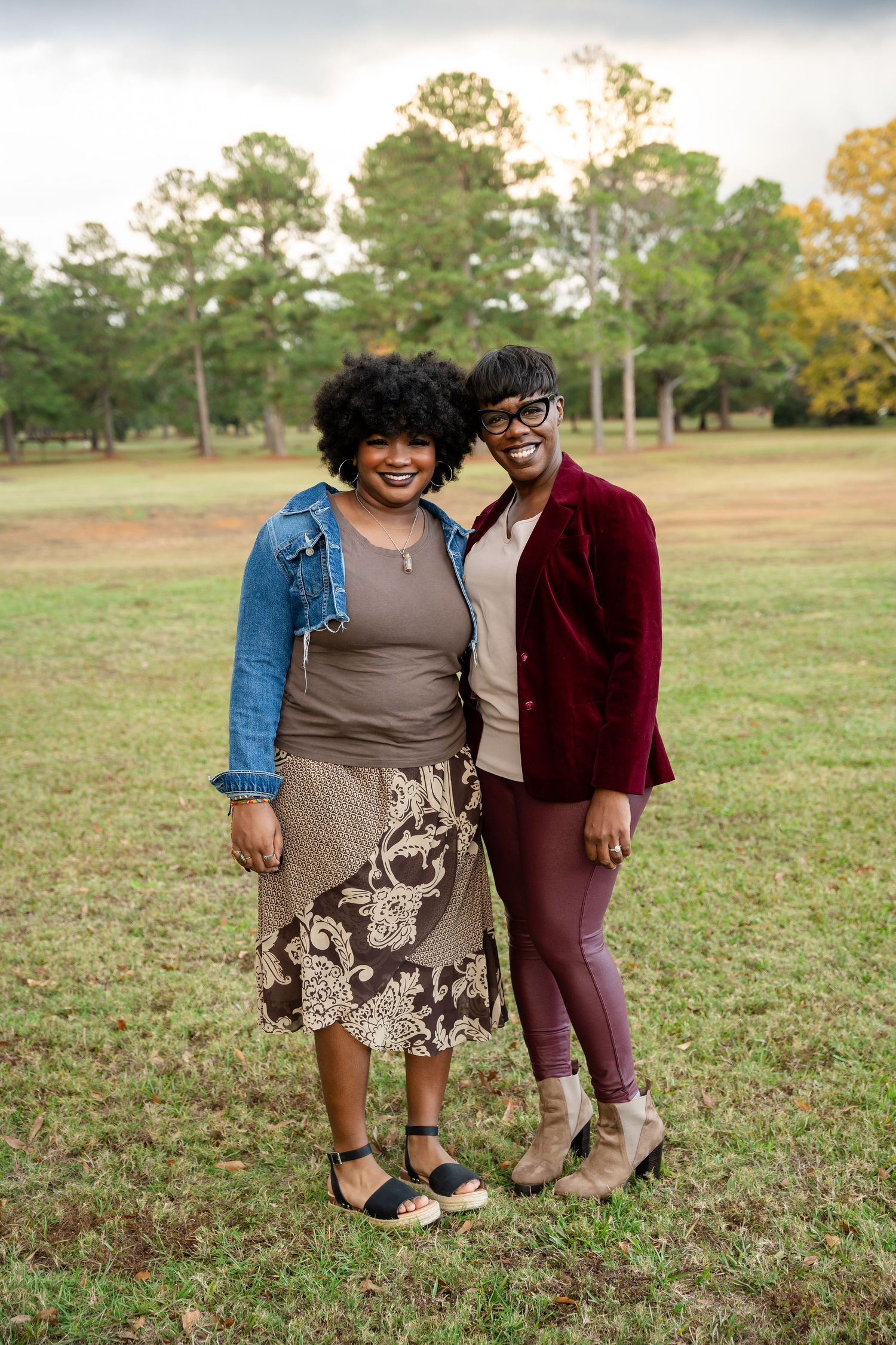 Two people sharing a joyful moment while posing together on grass with pine trees in background.