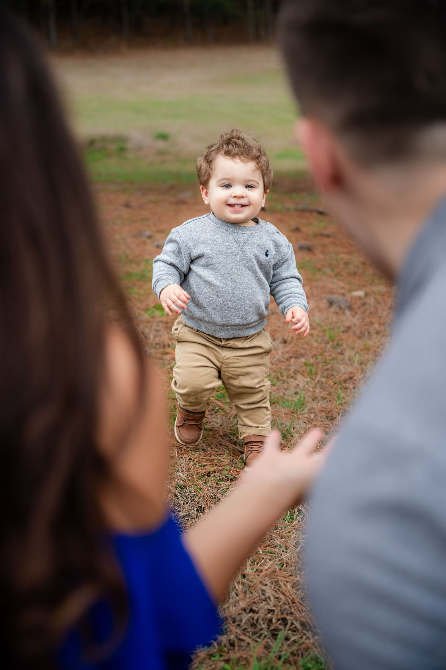 Young child in grey shirt and khaki pants running outdoors during family photoshoot.